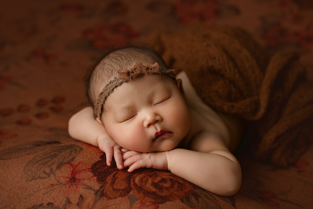 baby girl posed peacefully with her head resting on her hands on a orange floral backdrop