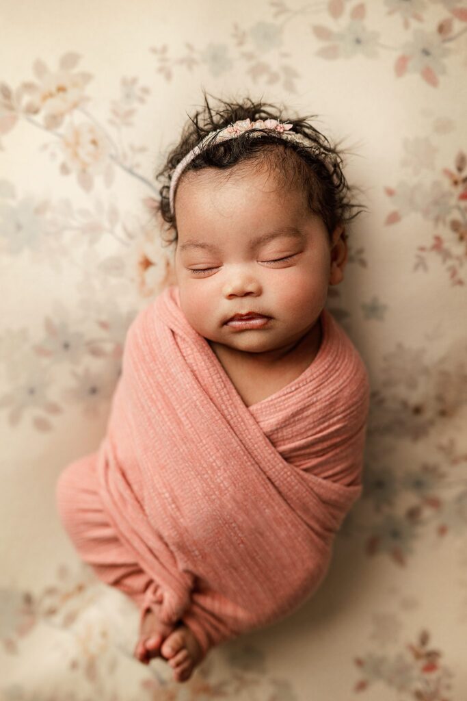 beautiful baby girl in pink wrap posed on floral backdrop at her newborn photoshoot with joan marie photography in scotch plains nj