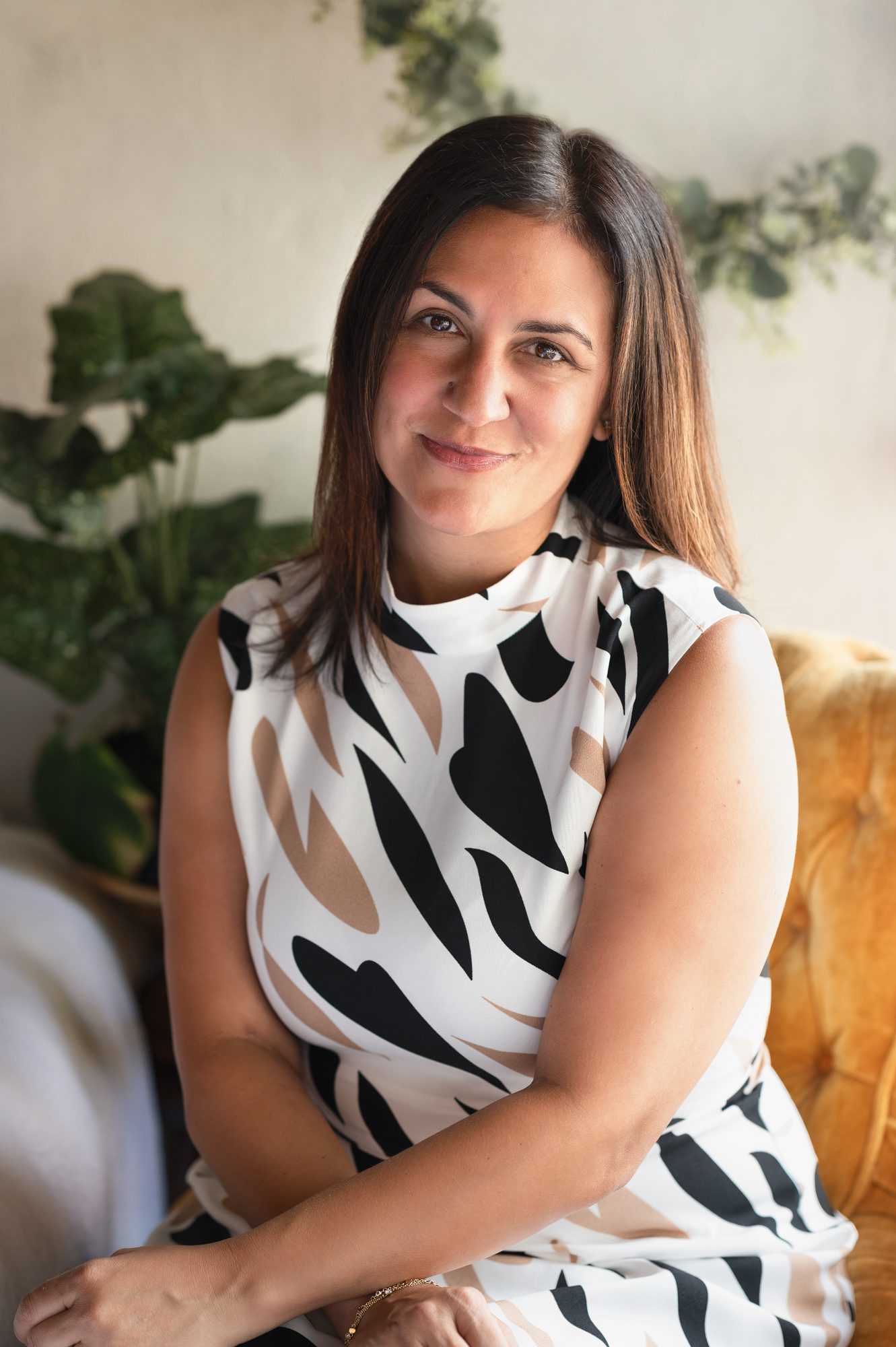 woman with brown hair poses on yellow chair for headshot