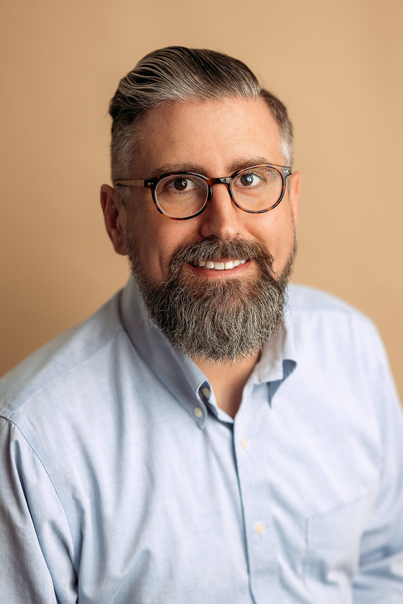 man poses for headshot in front of beige backdrop