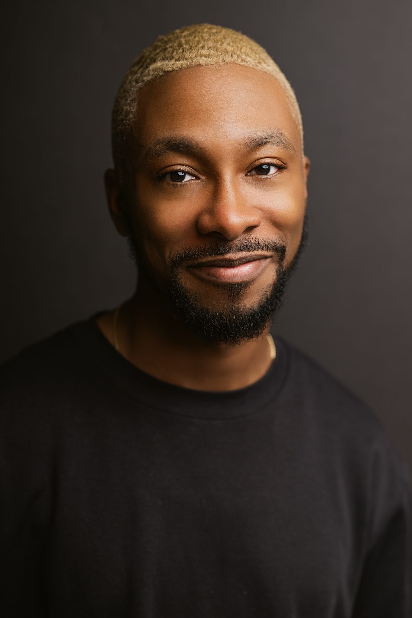 man in black shirt poses for headshot on black backdrop
