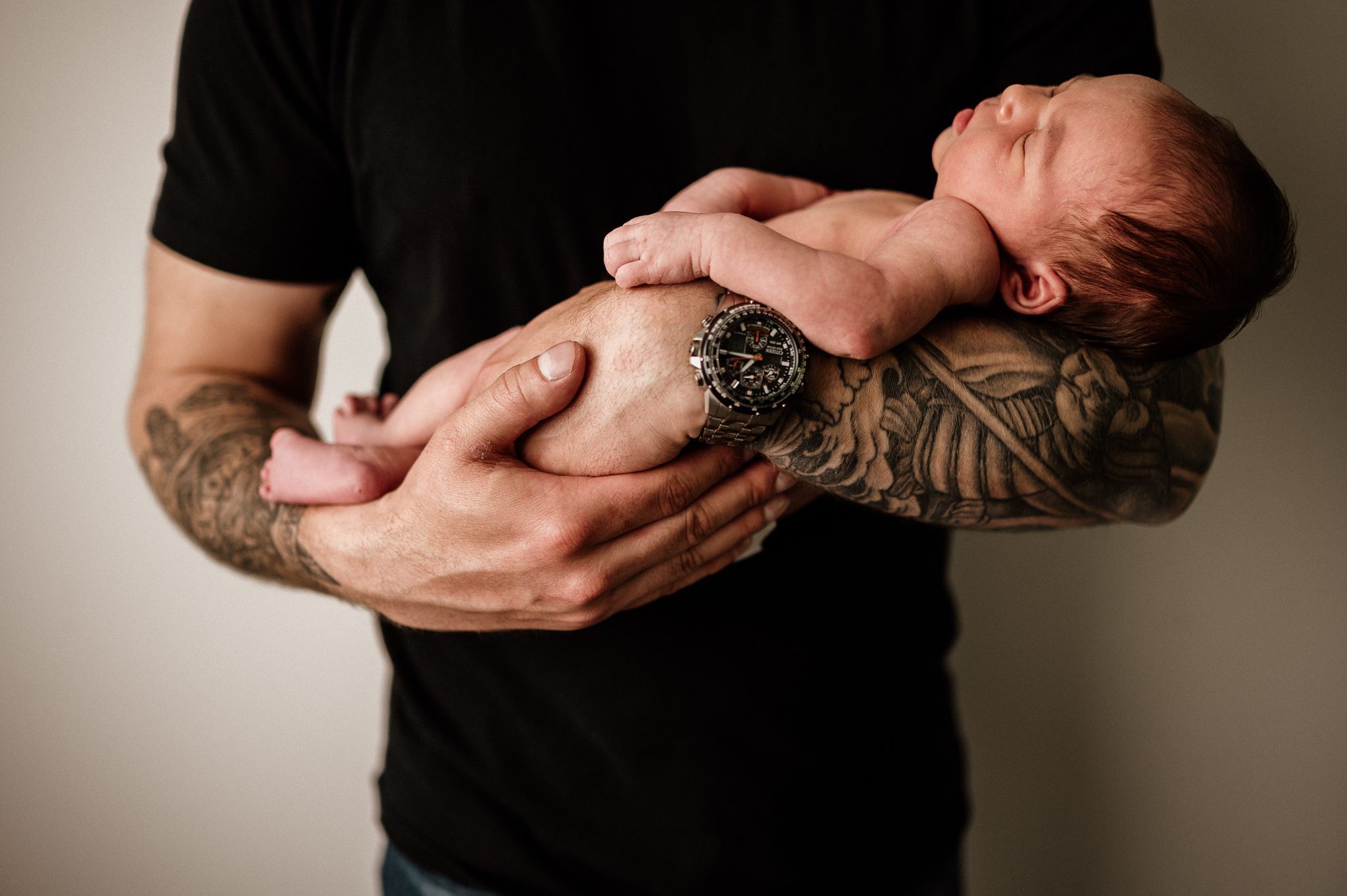 baby held in dad's tattooed arms