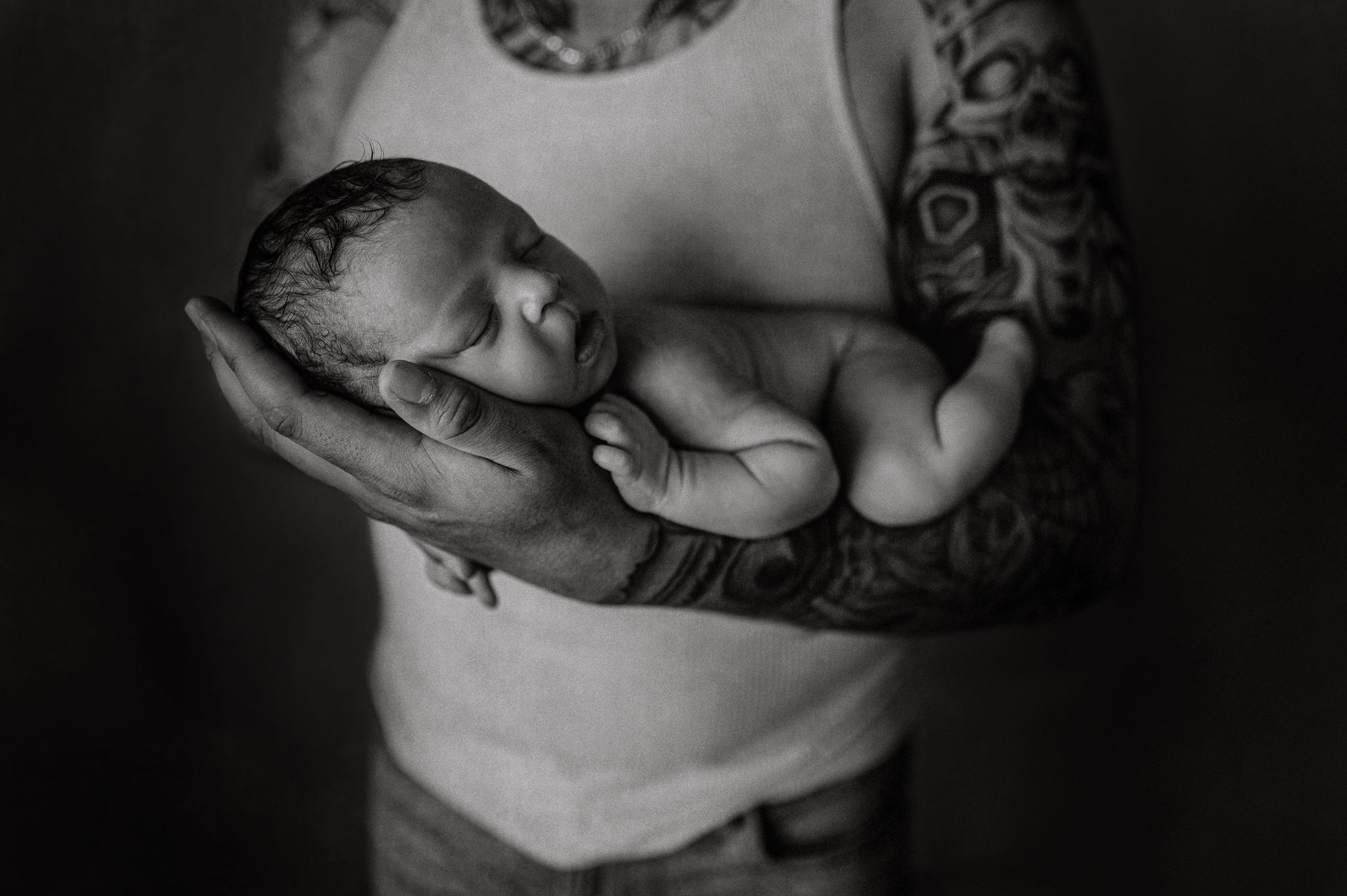 Close-up of a tattooed father holding his newborn son, showcasing a unique blend of body art and newborn photography in a Scotch Plains studio.