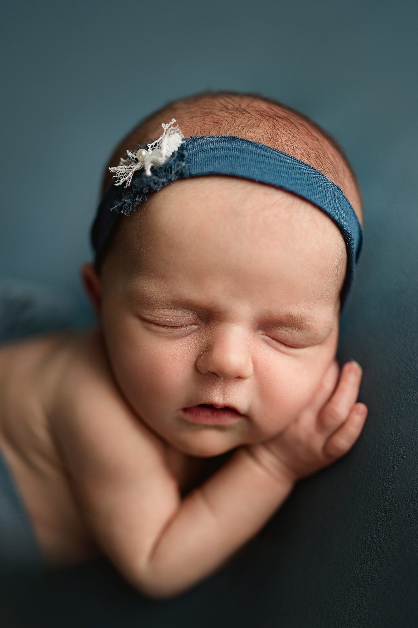 Newborn girl on blue backdrop sweetly sleeps during her studio newborn photography session with Joan Marie Photography in Scotch Plains