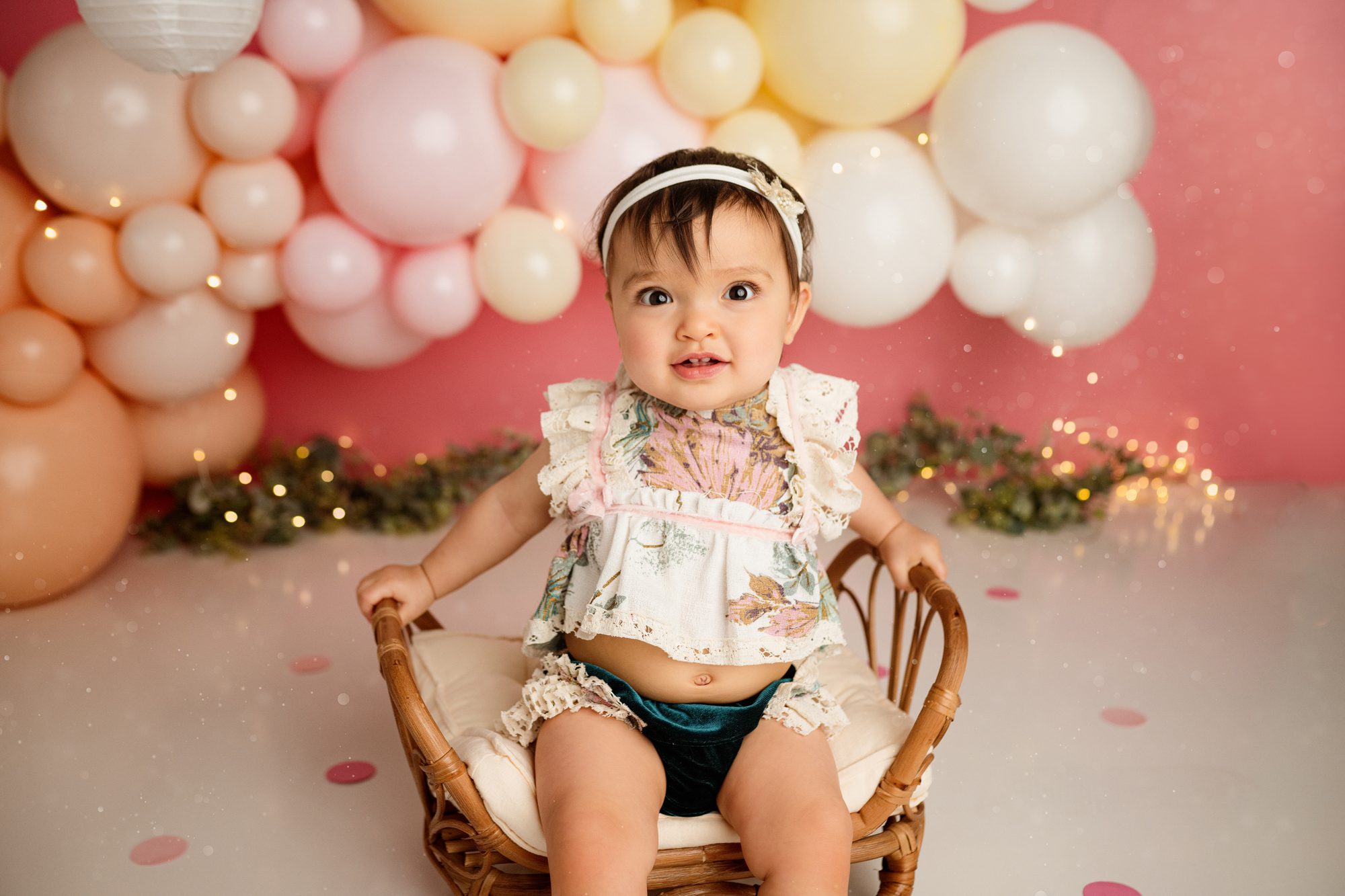adorable one year old poses for her first birthday cake smash session infront of balloons
