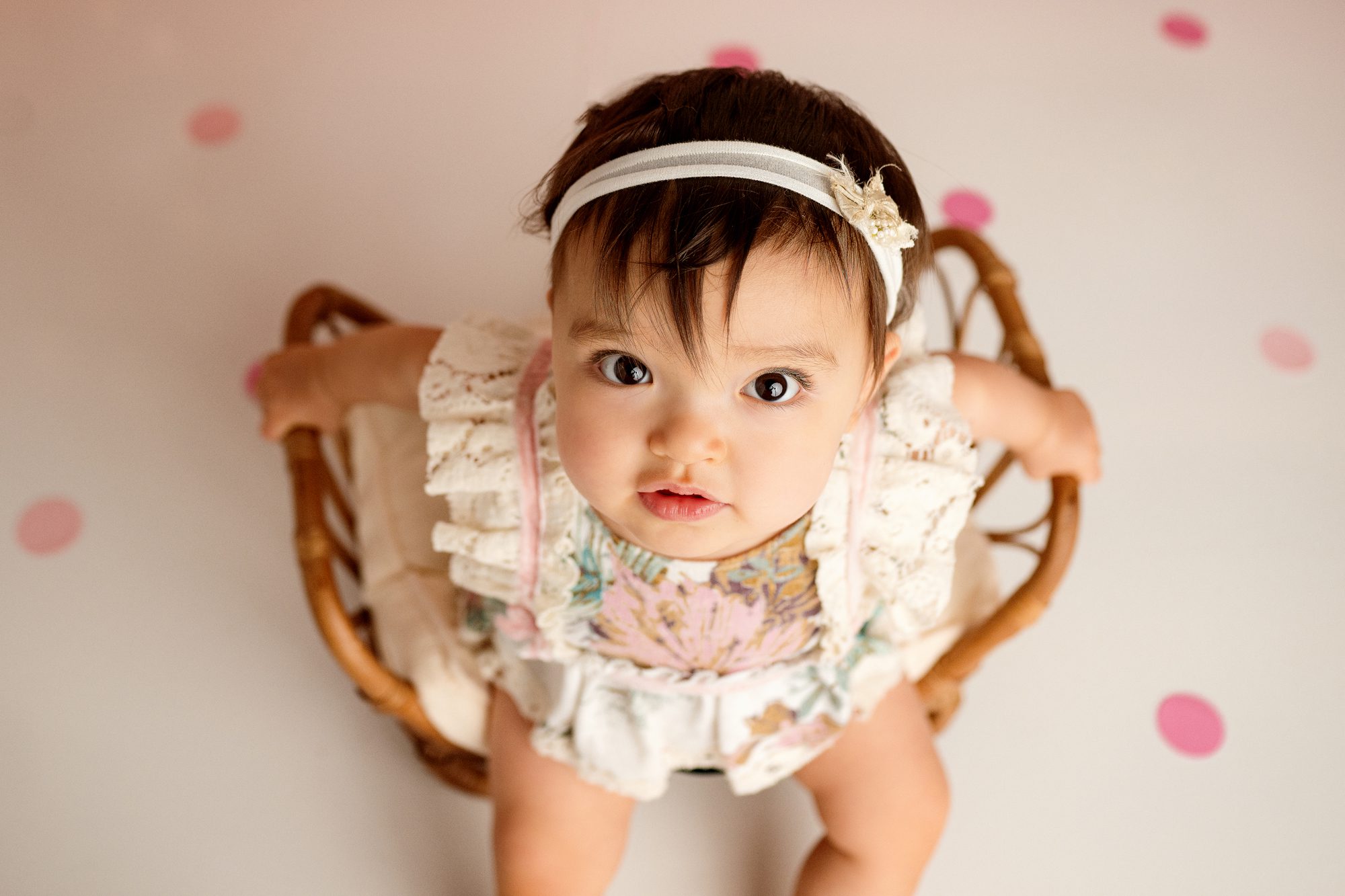 adorable one year old poses for her first birthday cake smash session infront of balloons