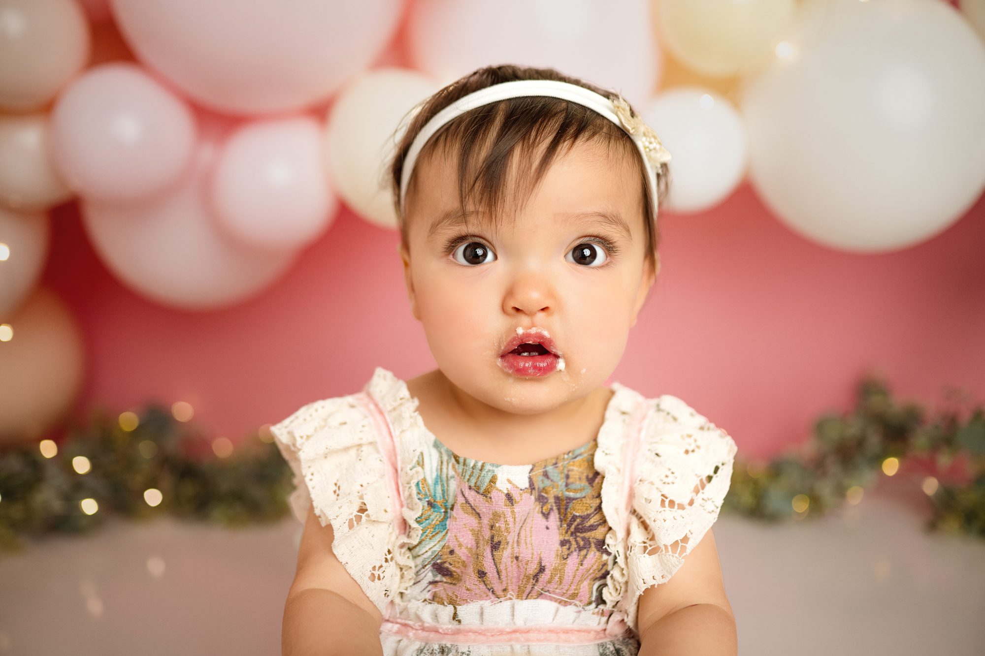 adorable one year old poses for her first birthday cake smash session infront of balloons