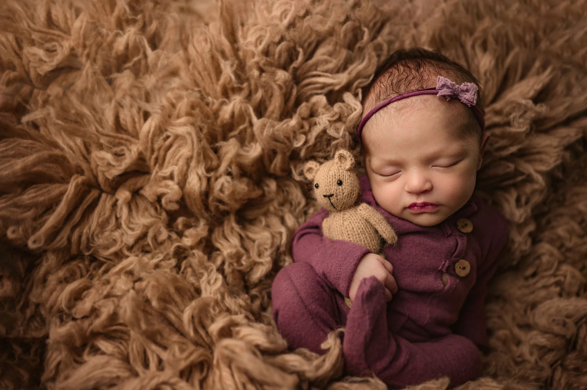 newborn baby in purple footed romper posed on a tan fur
