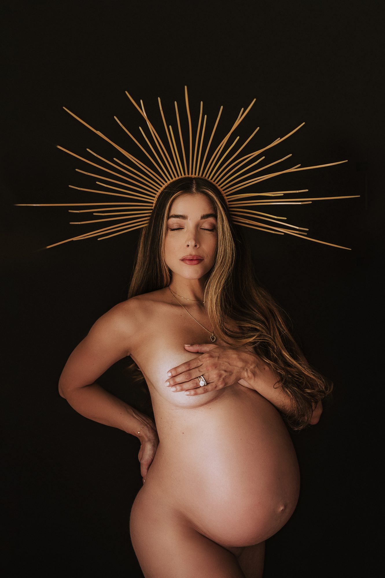 beautiful mother to be poses with golden grown on her head in this maternity portrait