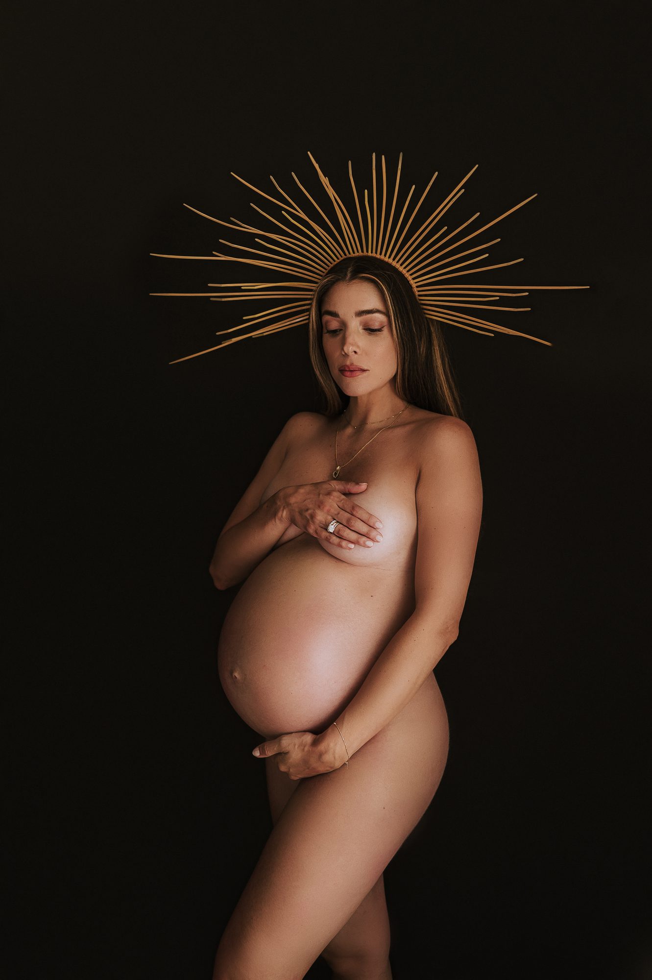 beautiful mother to be poses with golden grown on her head in this maternity portrait