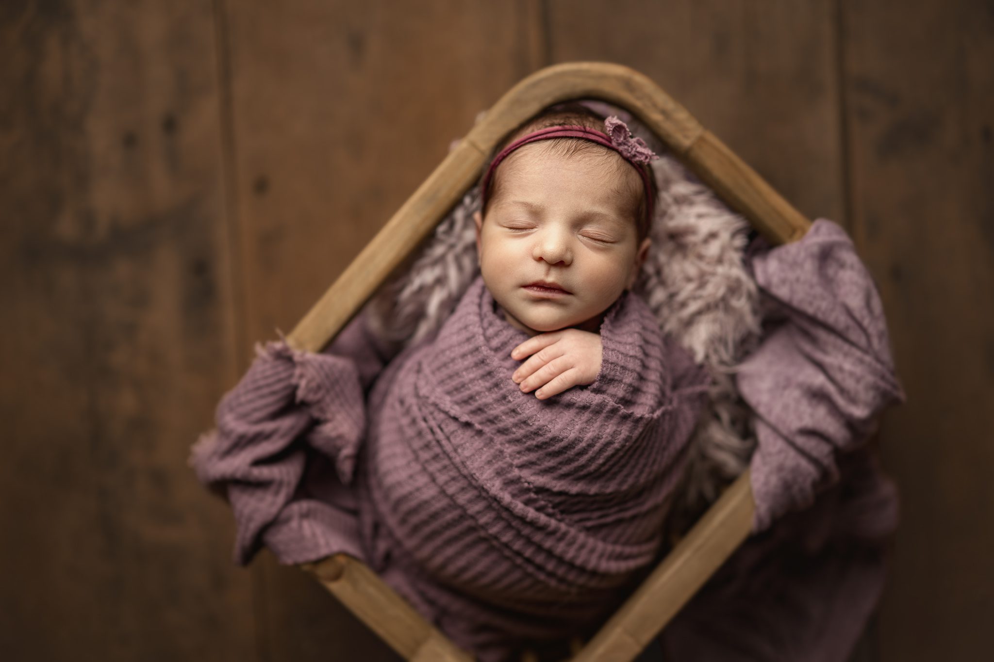 newborn baby girl in a wooden crate sleeping with a little bow on her head