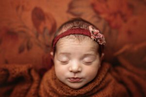 newborn baby girl in rust colored fabric on a floral backdrop with little puckered lips
