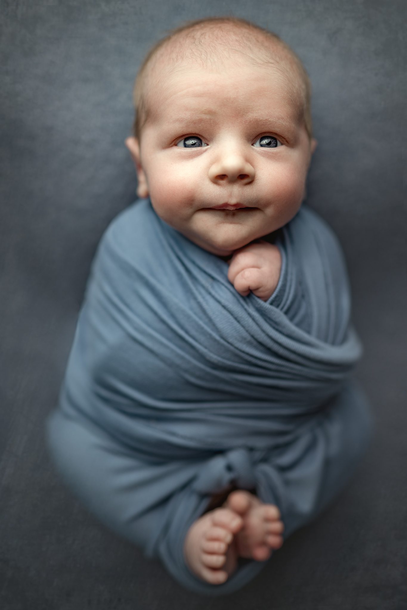 baby boy swaddled in blue fabric looks up at the camera