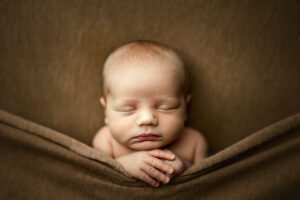 photo of a newborn baby boy tucked into a brown sheet