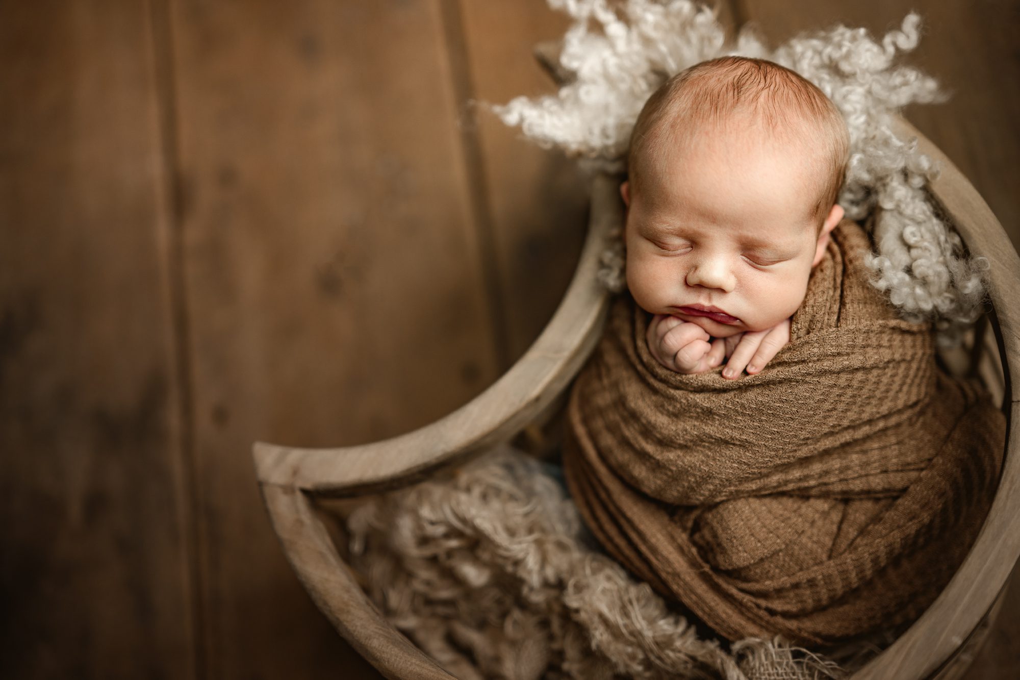newborn baby boy posed in a wooden moon shaped bowl