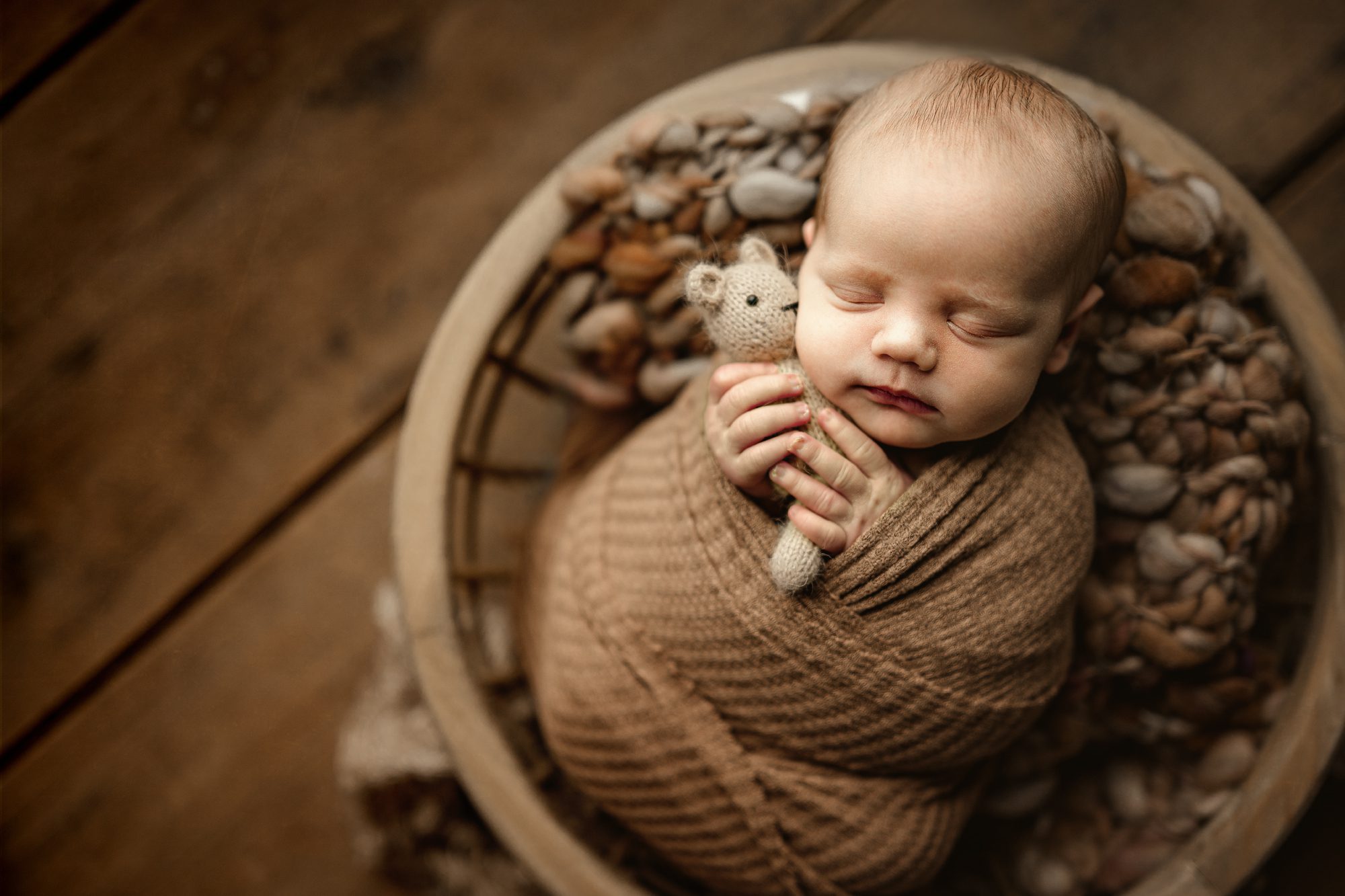 newborn baby boy posed in a wooden bowl holding a little teddy bear