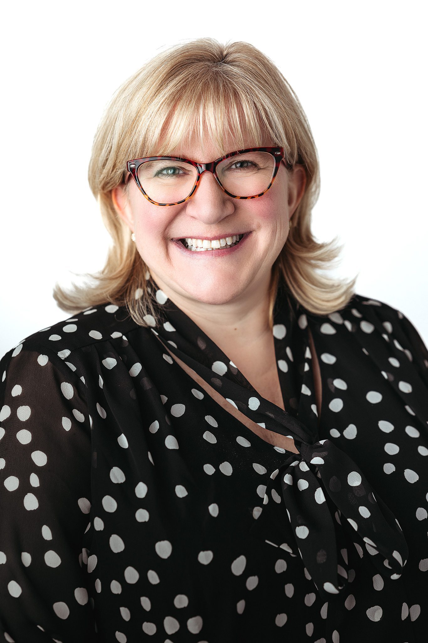 blonde woman in polka dot shirt posing for her headshot on a white backdrop