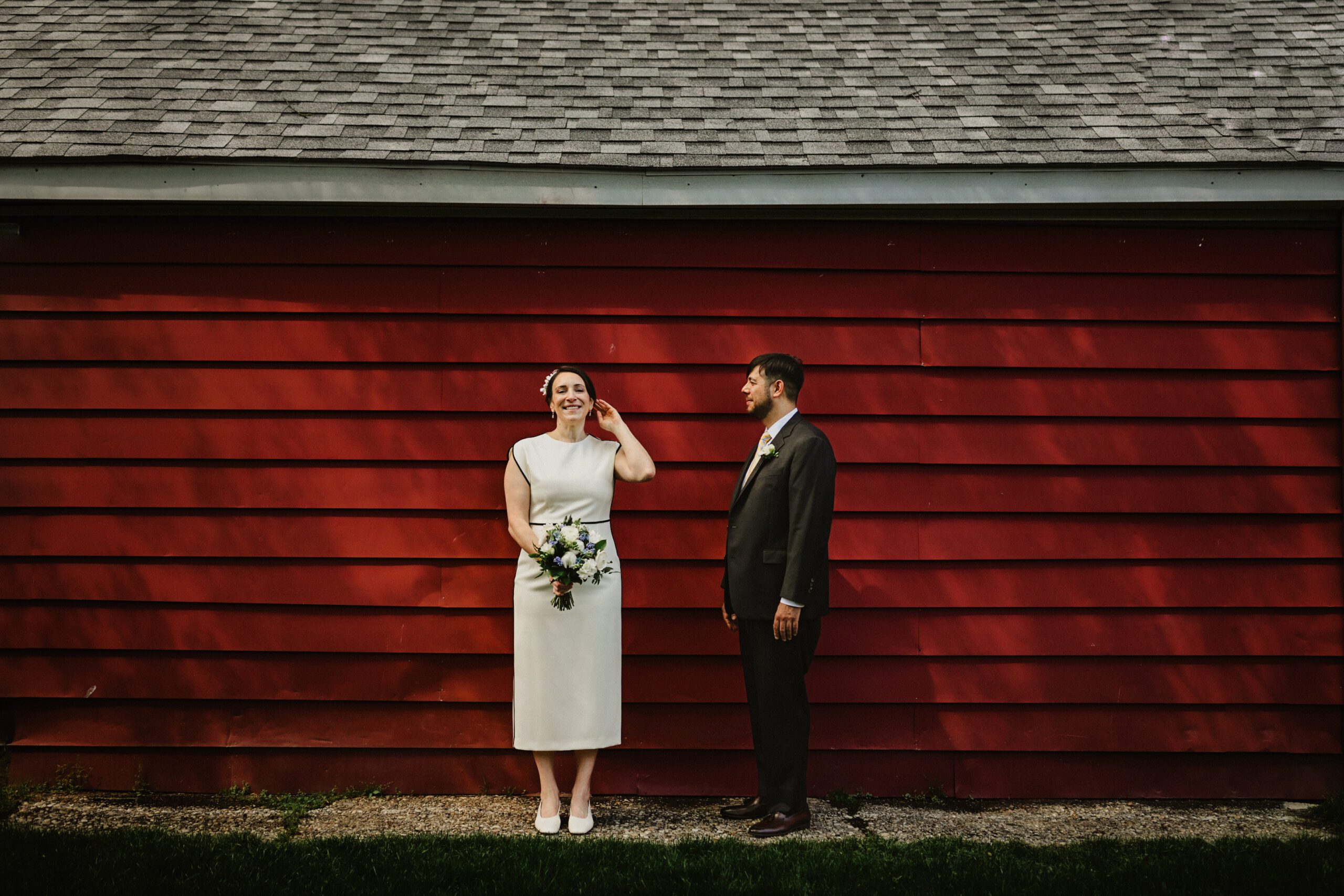 bride and groom take candid portrait in front of red bard with dappled light