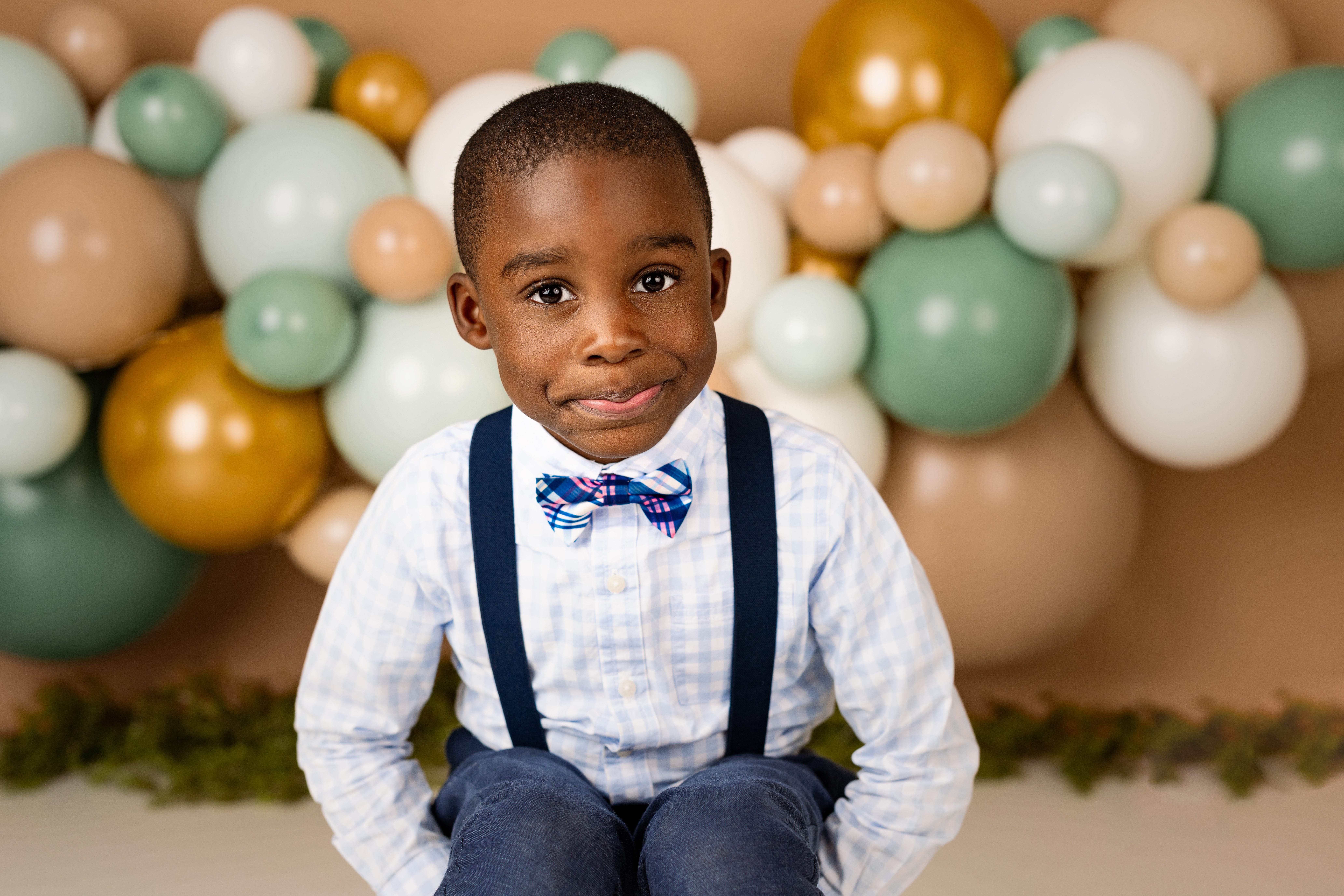 Little boy smiles infront of balloon garland for nj newborn photographer