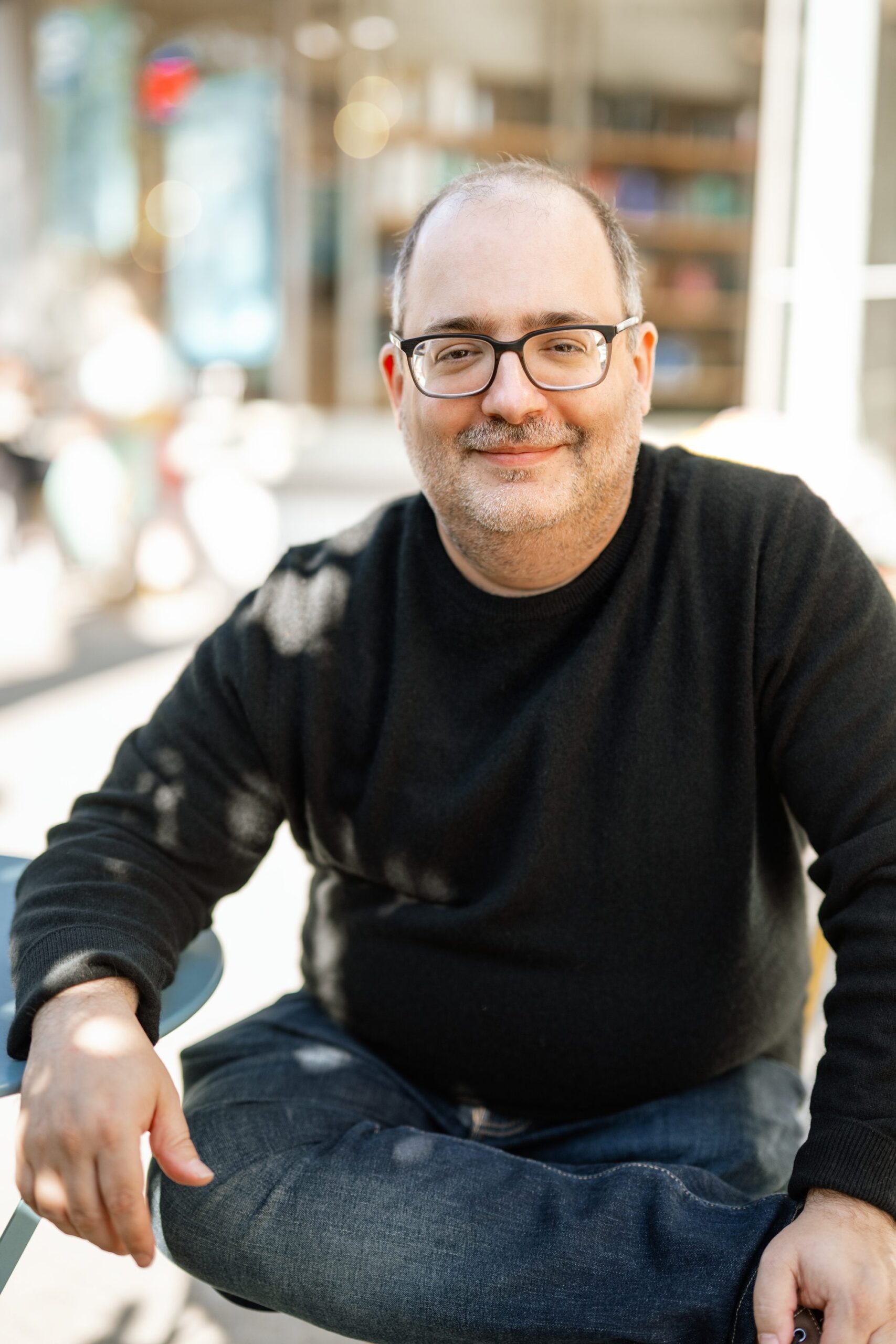 man in black sweater and jeans sits in a relaxed pose outside for his dating profile session in Morristown NJ with Joan Marie Photography