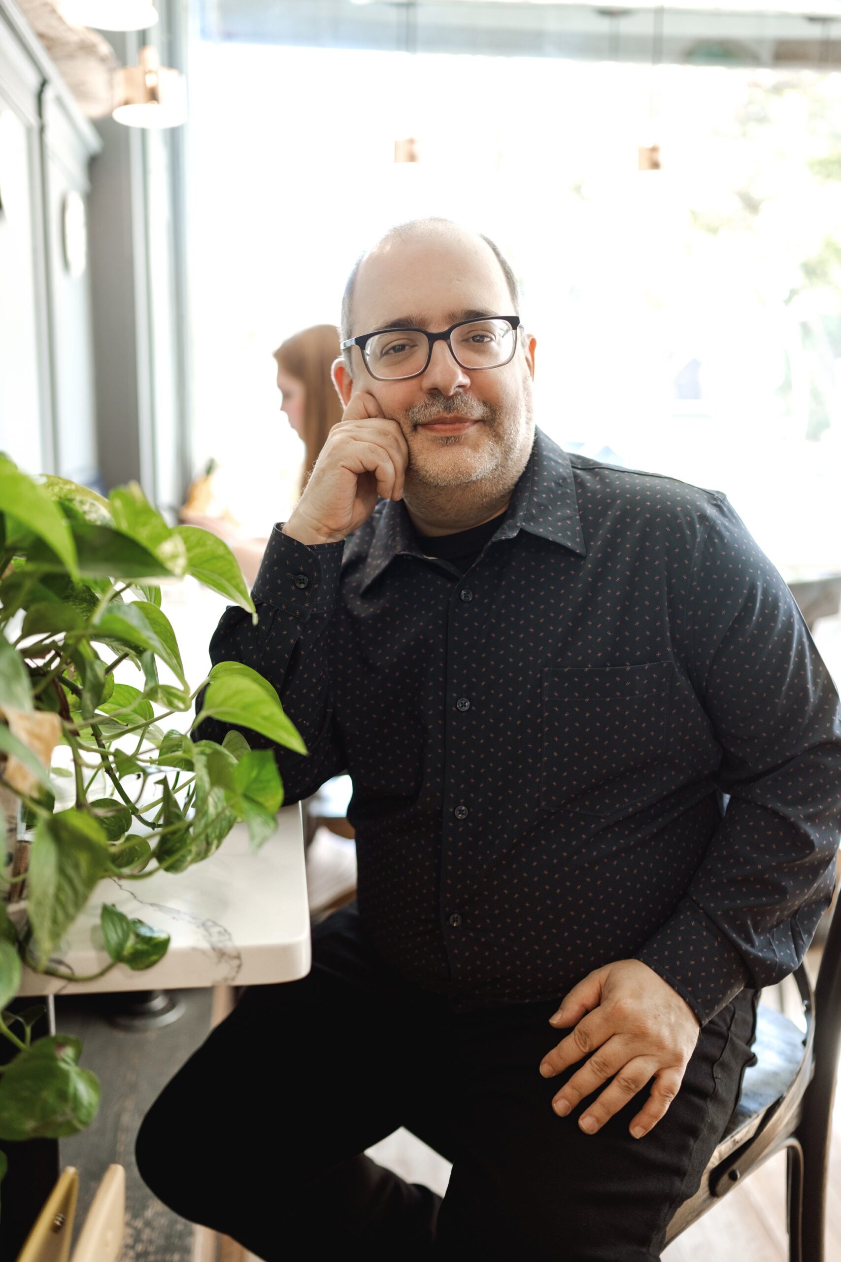 man in nice button down shirt sits in a relaxed pose at LOKL Coffee for his dating profile session in Morristown NJ with Joan Marie Photography