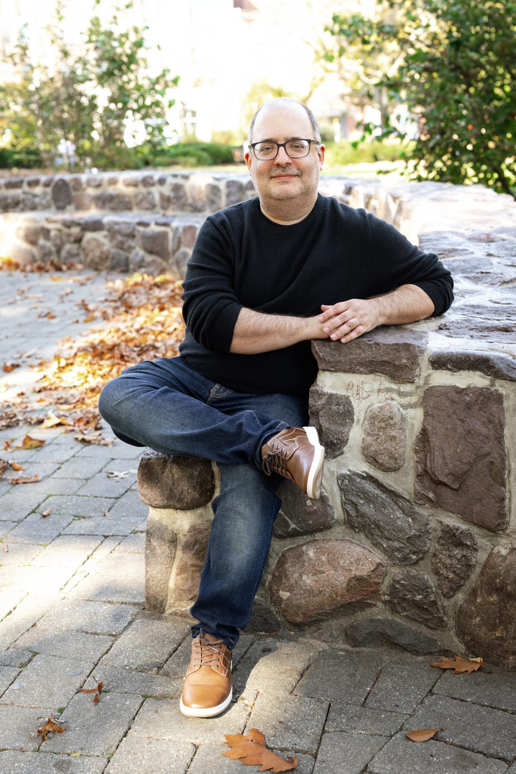 man in black sweater and jeans sits in a relaxed pose outside for his dating profile session in Morristown NJ with Joan Marie Photography