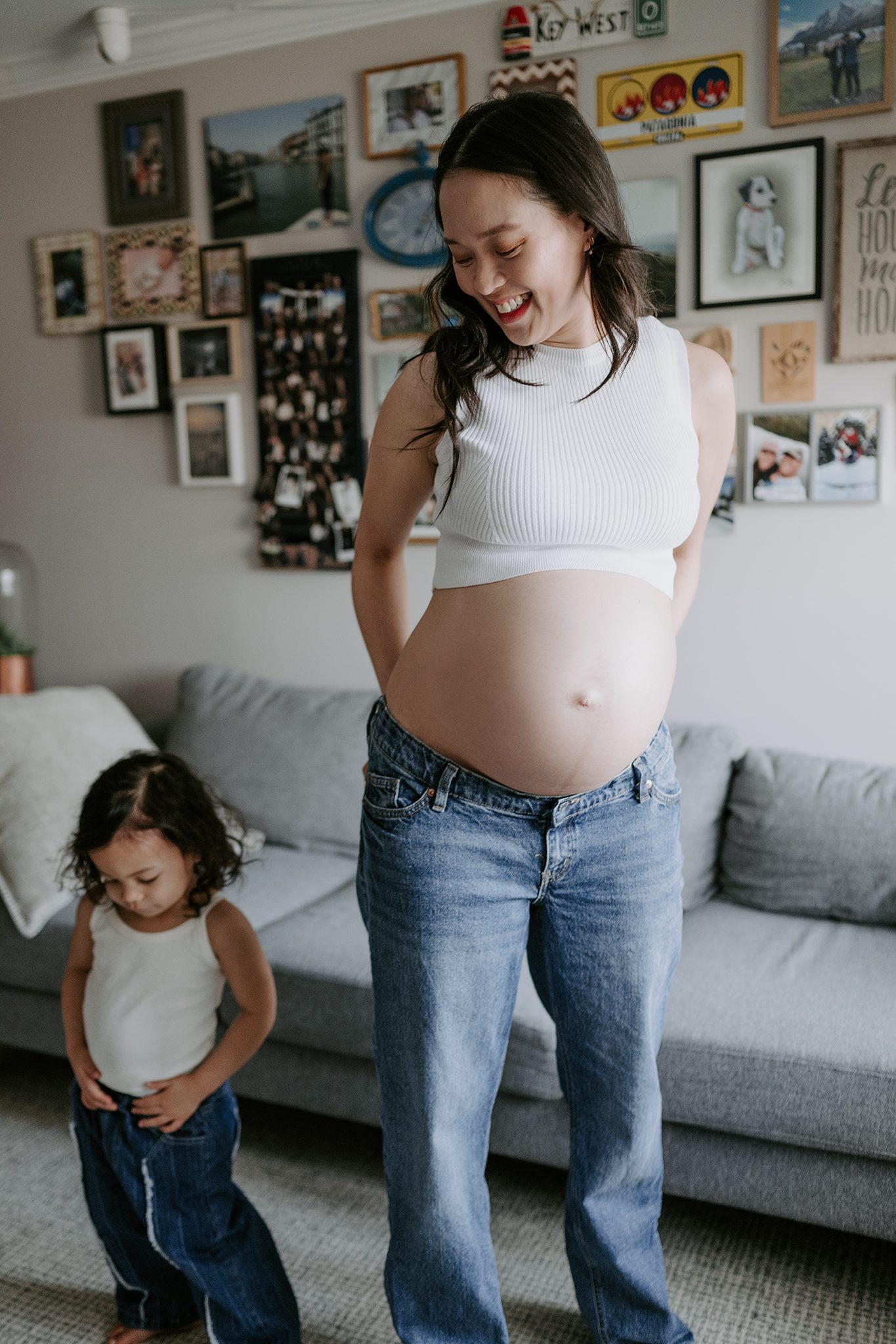 mother and daughter in matching jeans and white tank tops dance in their den together during their in-home maternity session in scotch plains nj with joan marie photography