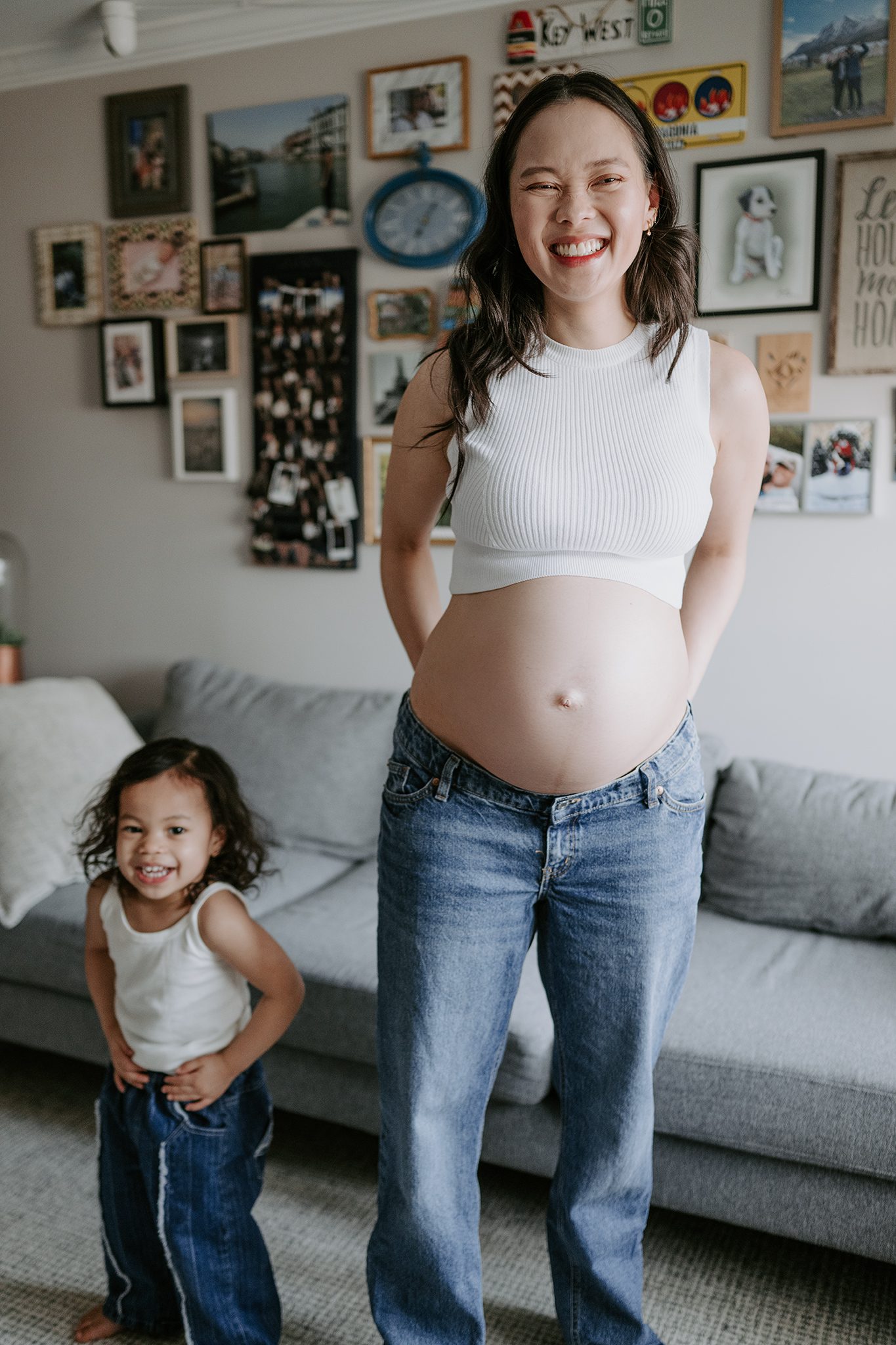 mother and daughter in matching jeans and white tank tops dance in their den together during their in-home maternity session in scotch plains nj with joan marie photography