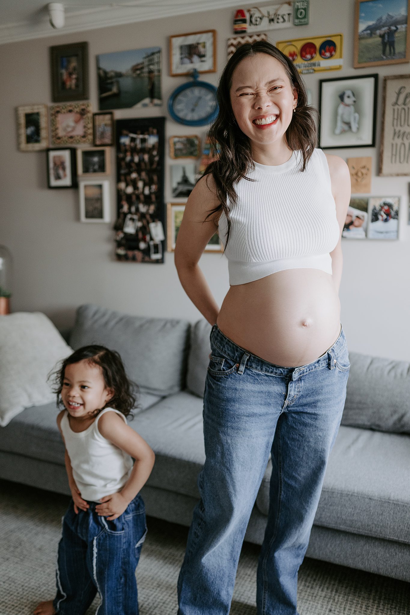 mother and daughter in matching jeans and white tank tops dance in their den together during their in-home maternity session in scotch plains nj with joan marie photography