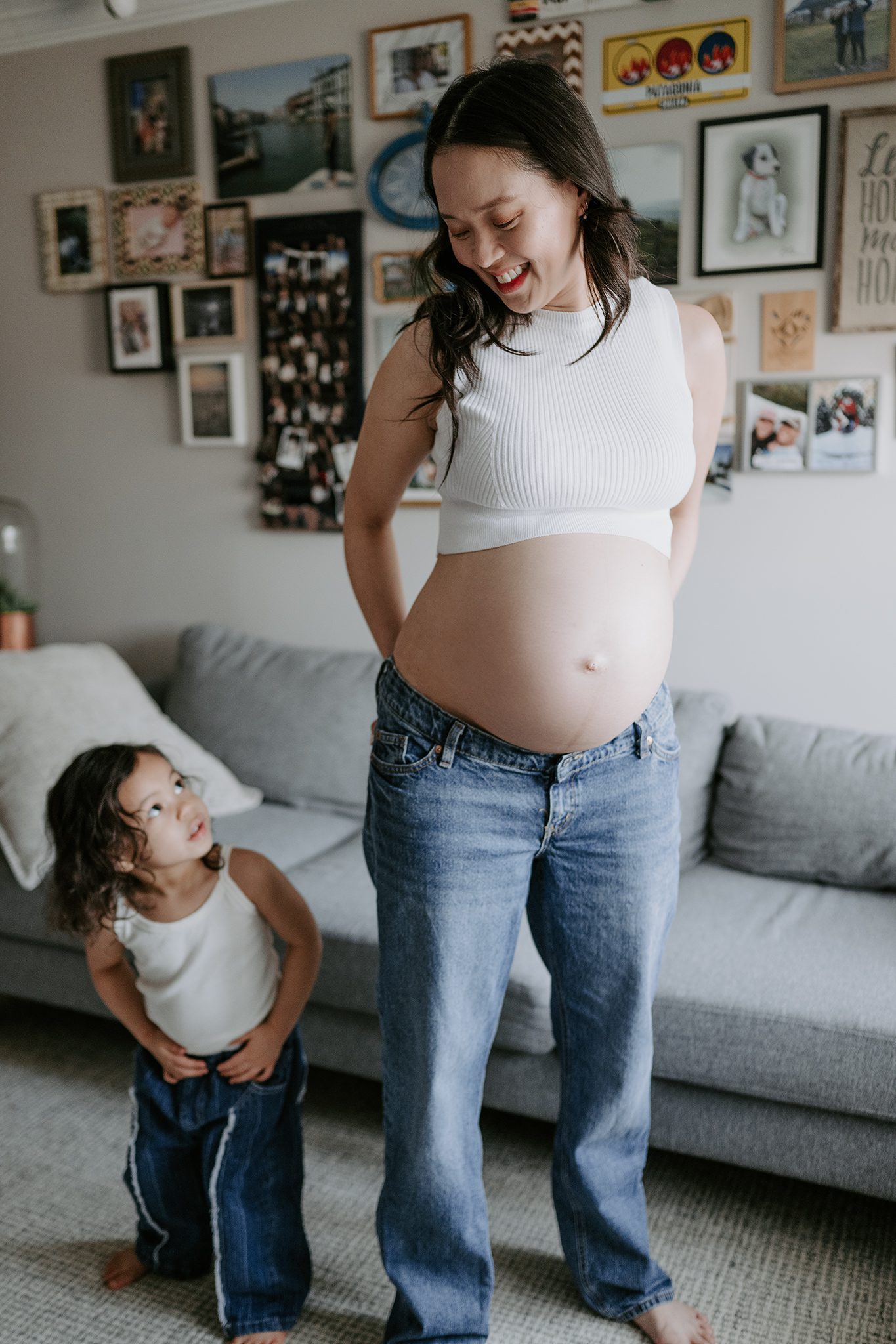 mother and daughter in matching jeans and white tank tops dance in their den together during their in-home maternity session in scotch plains nj with joan marie photography