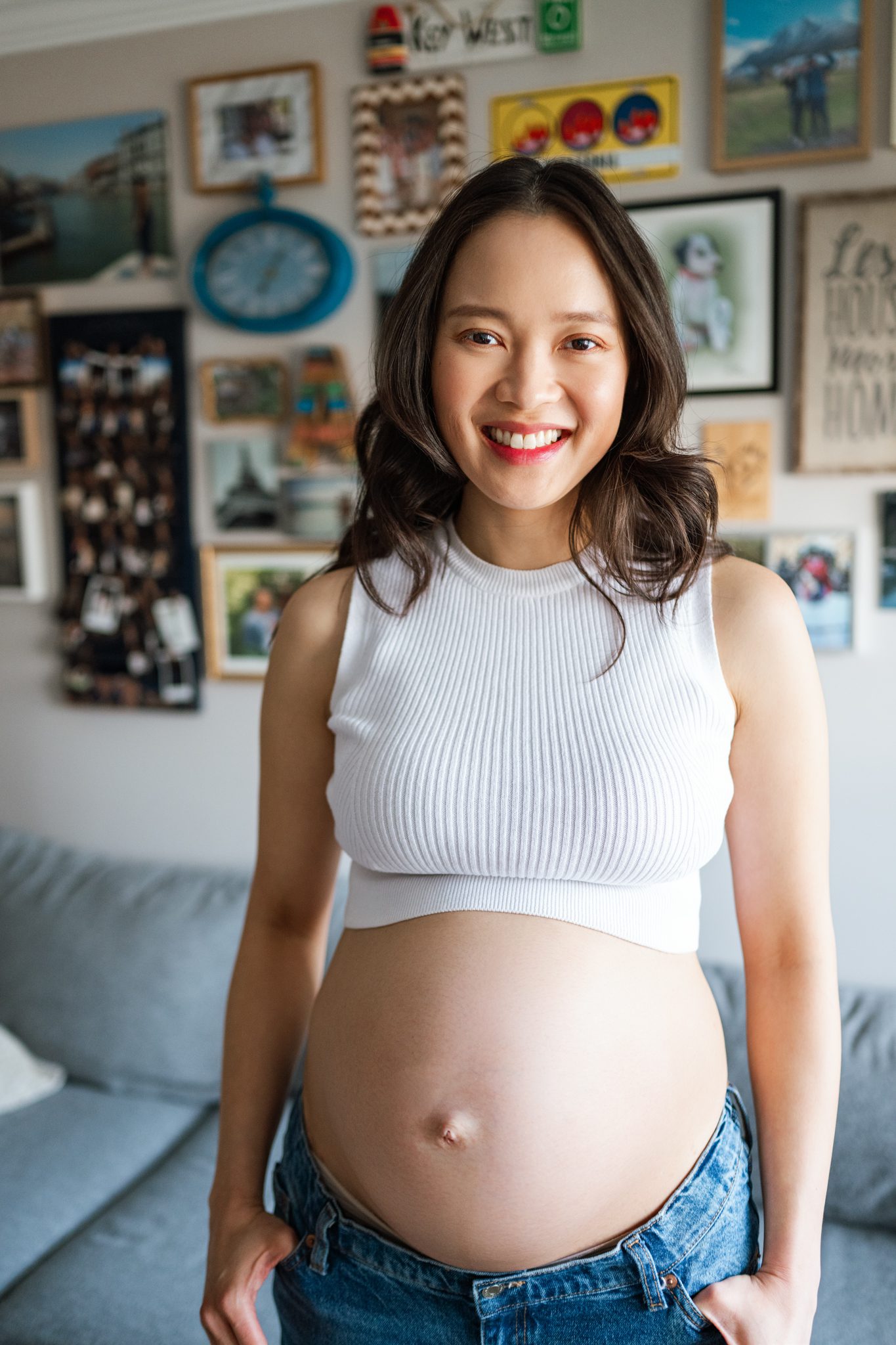 woman in a white tank-top and jeans smiles at her in home maternity session taken in scotch plains nj with joan marie photography