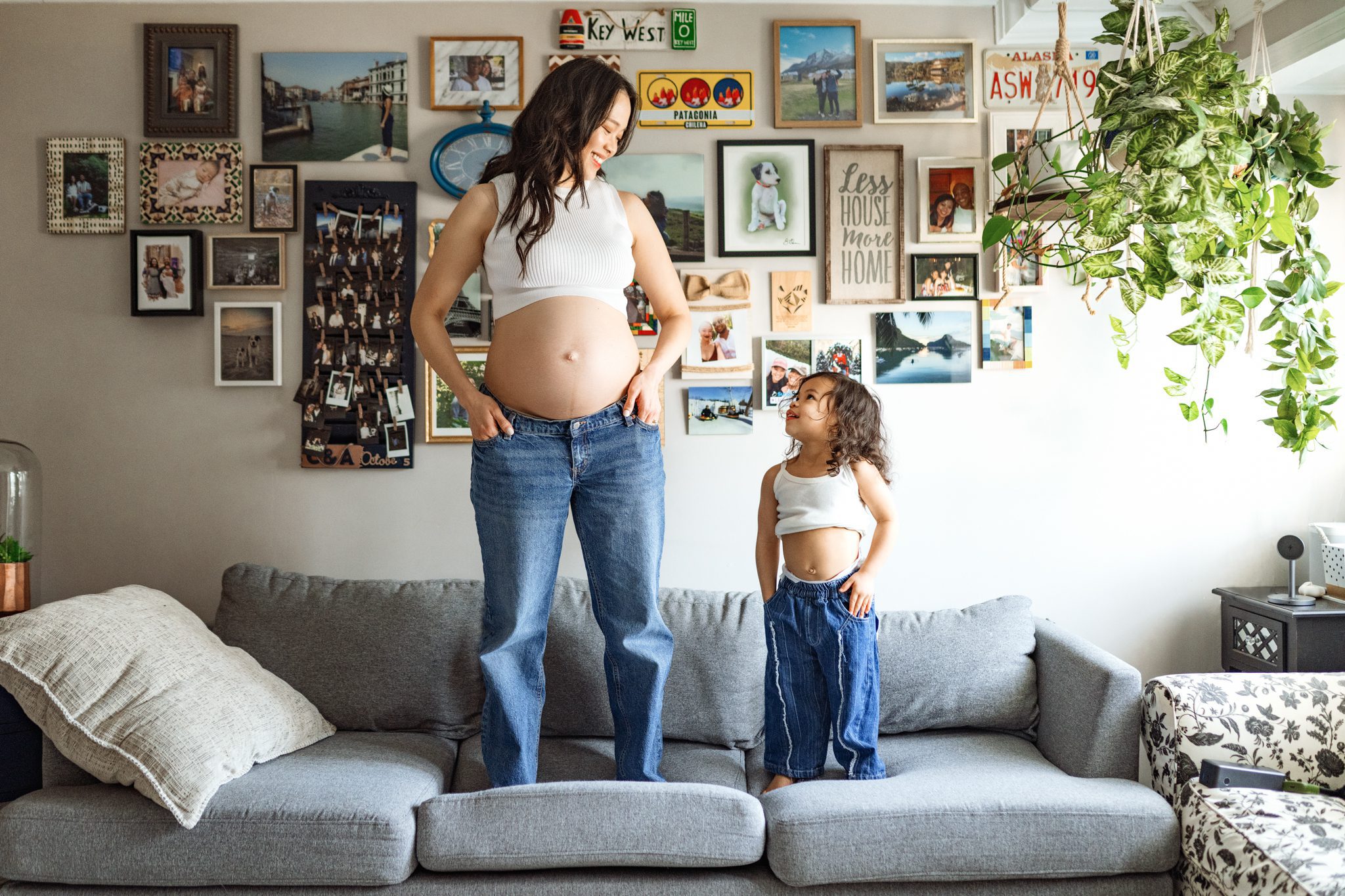 woman in a white tank-top and jeans smiles at her daughter at her in home maternity session taken in scotch plains nj with joan marie photography