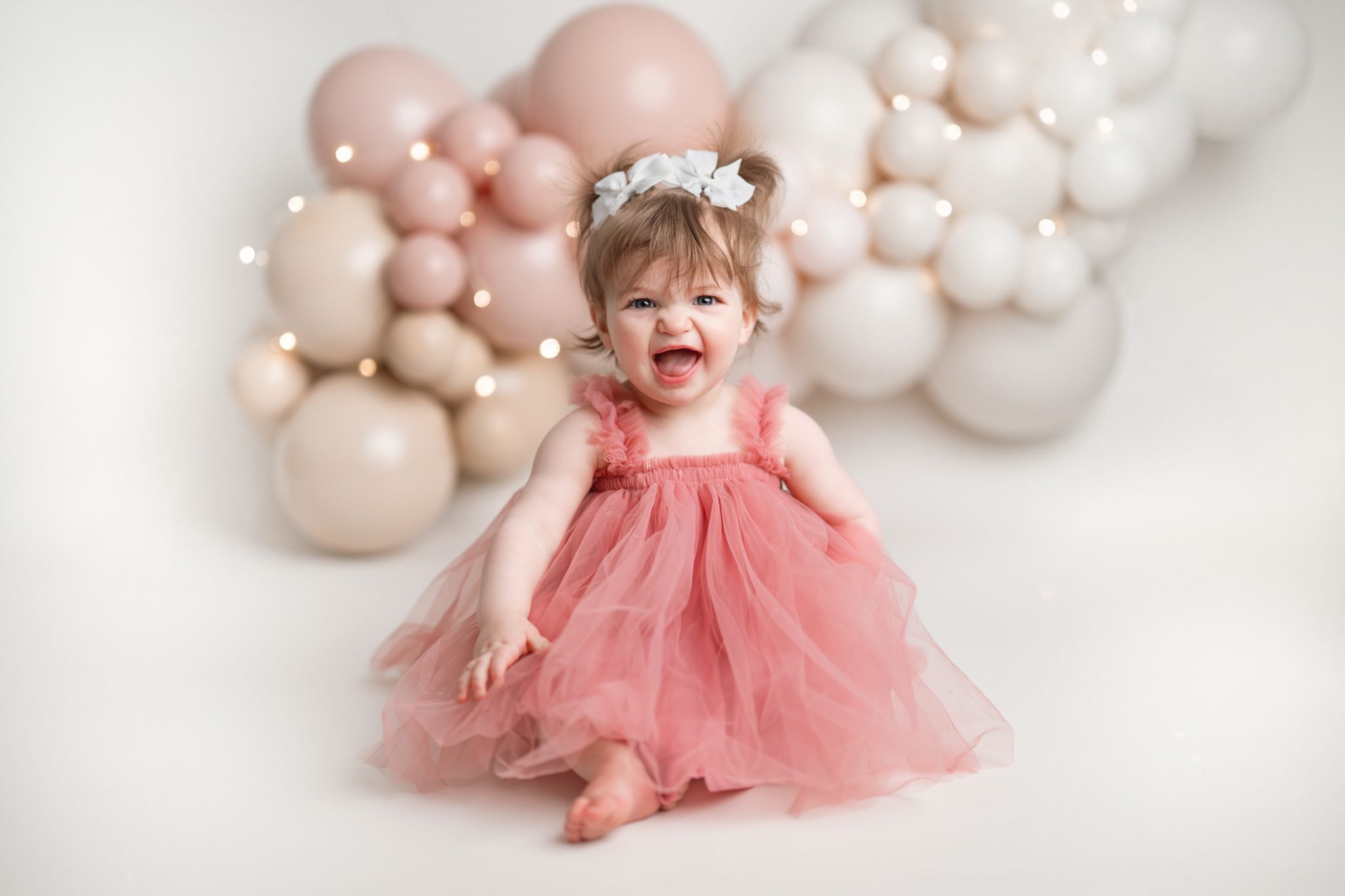 1 year old girl smiles big for the camera at her cake smash session with Joan Marie Photography