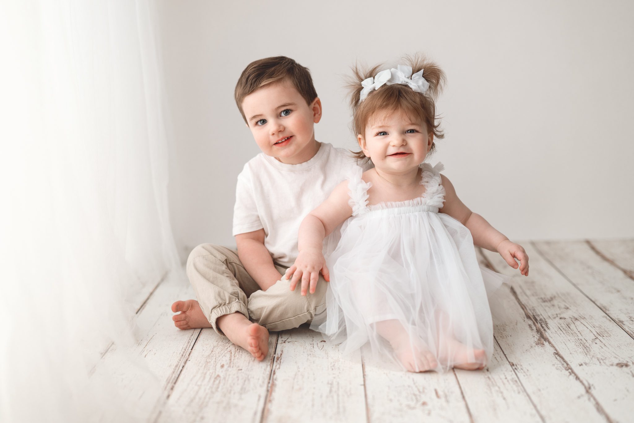 Toddler boy and baby girl sitting together for a first birthday cake smash with siblings in Scotch Plains.