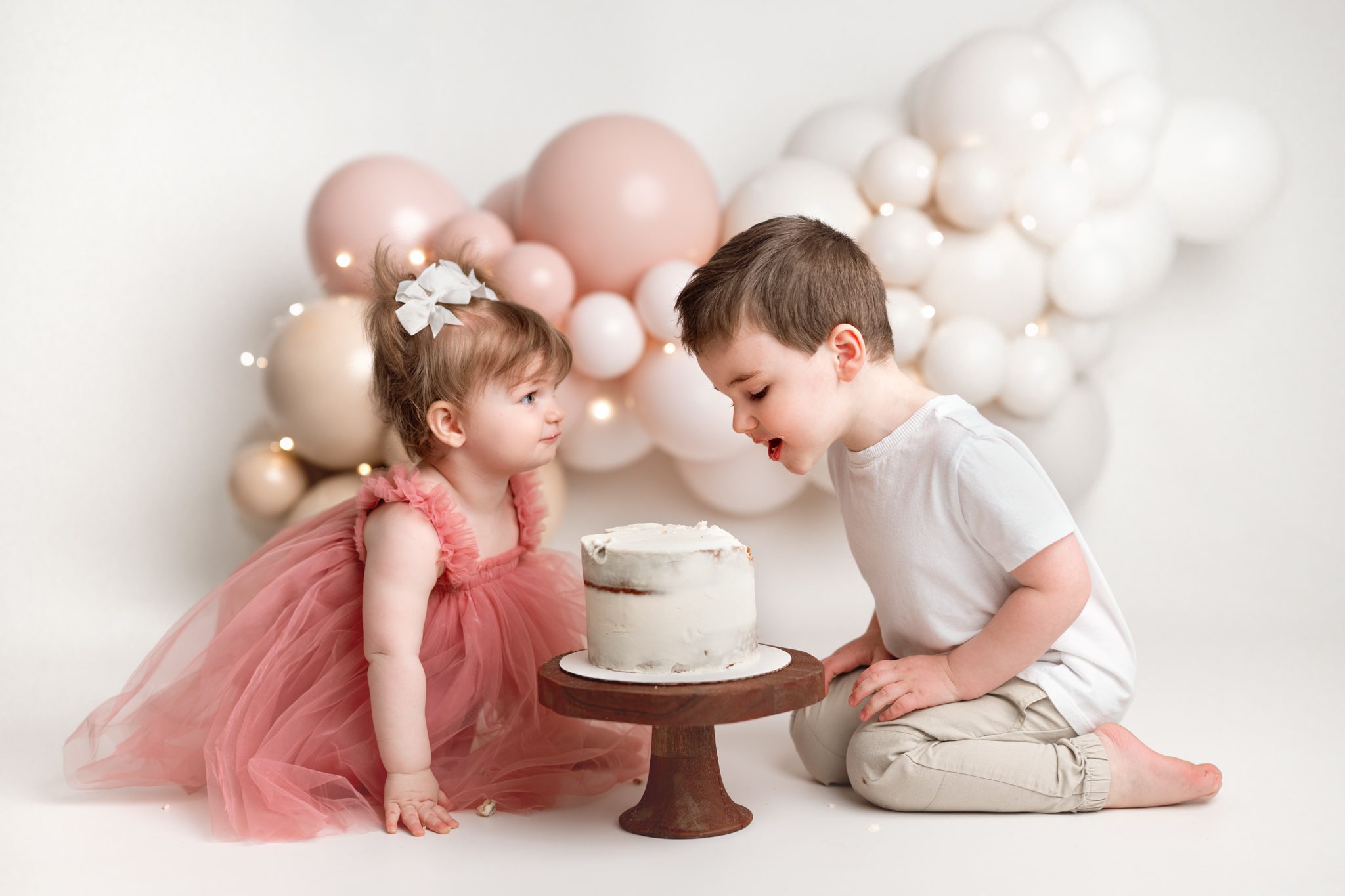 Three year old brother eating cake to help his sister during a first birthday cake smash with siblings in Scotch Plains.