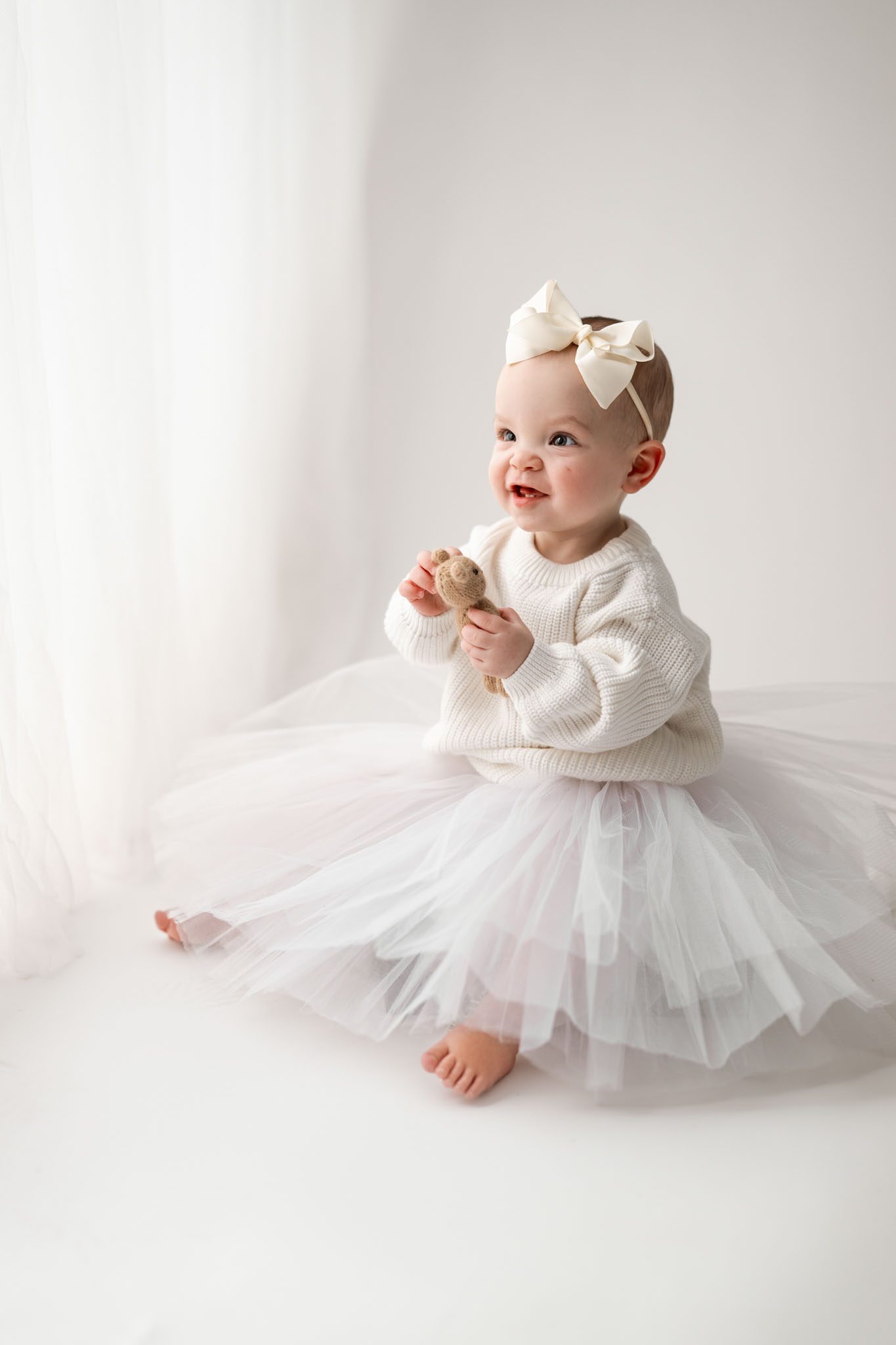Toddler wearing a white knit sweater and tulle skirt for a formal first birthday portrait on a white background.