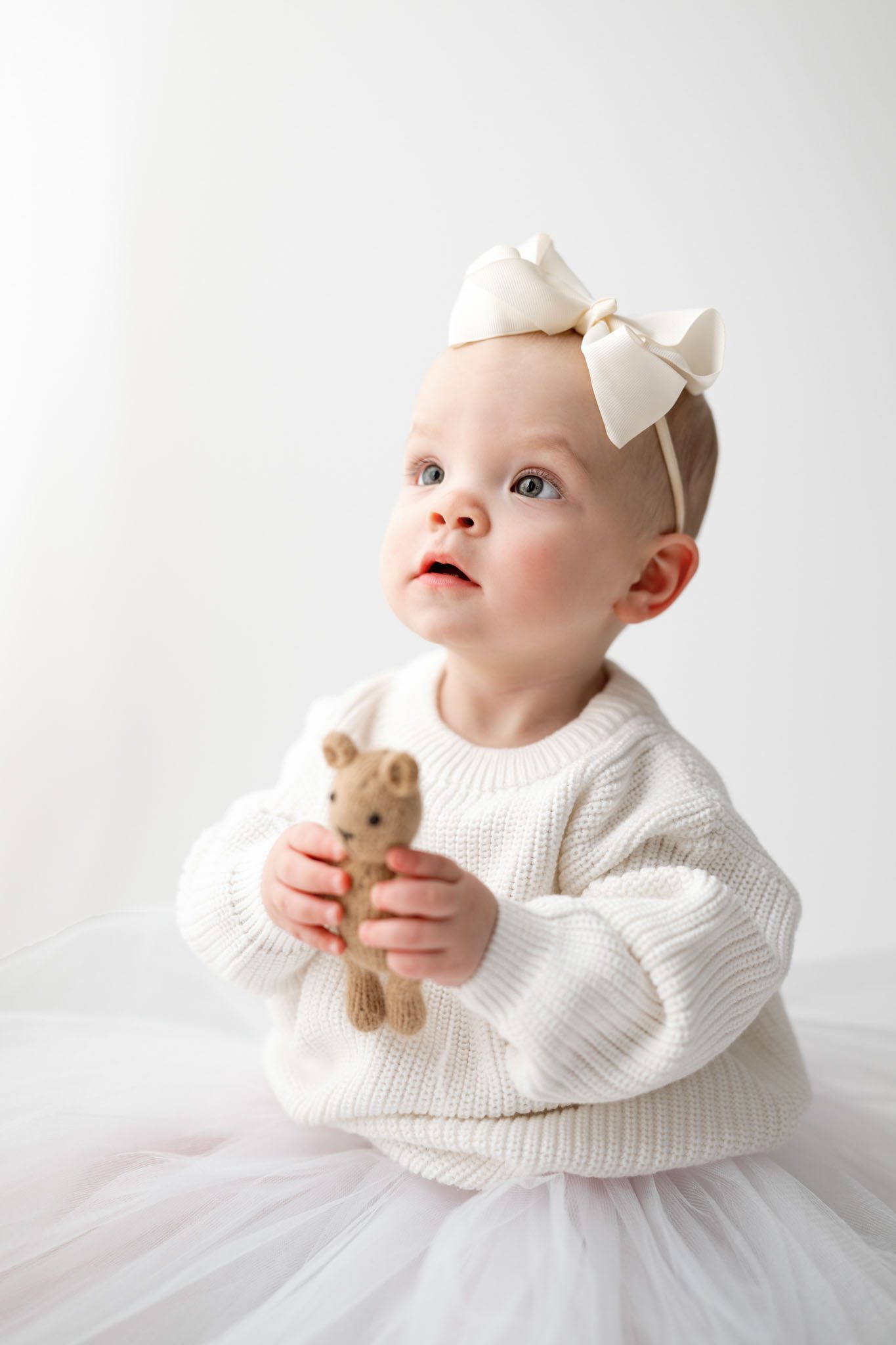 Toddler wearing a white knit sweater and tulle skirt for a formal first birthday portrait on a white background.