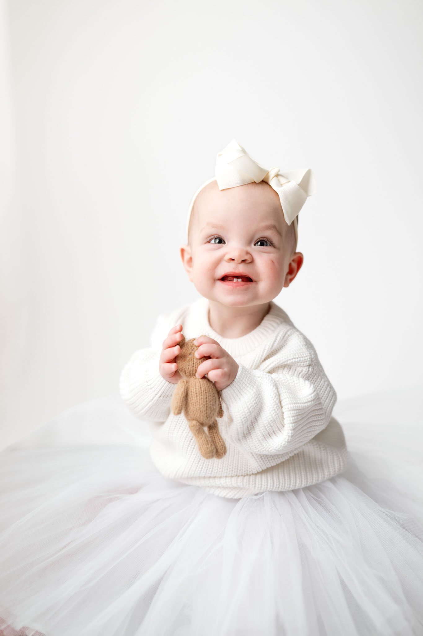 Toddler wearing a white knit sweater and tulle skirt for a formal first birthday portrait on a white background.