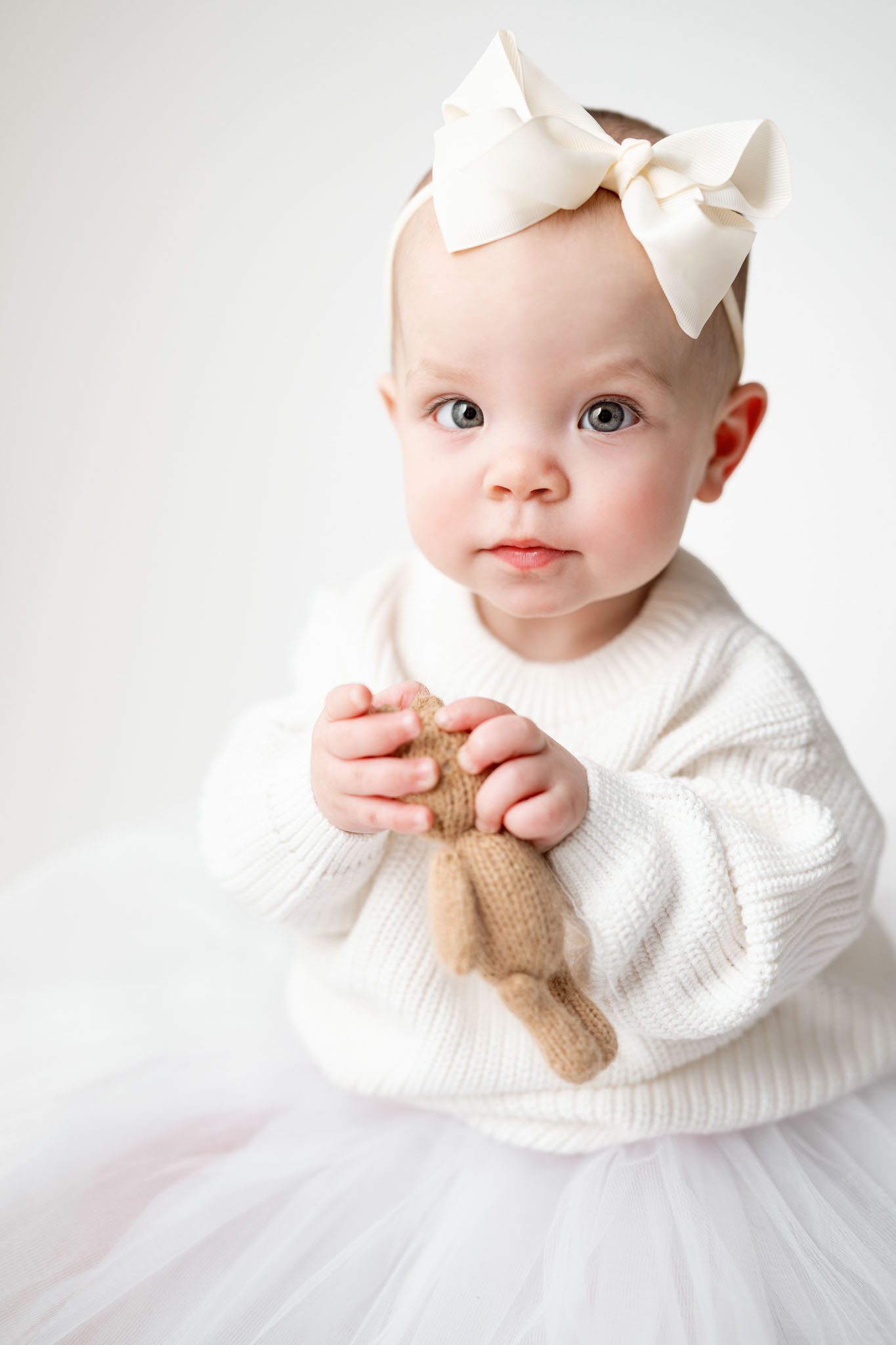 Toddler wearing a white knit sweater and tulle skirt for a formal first birthday portrait on a white background.