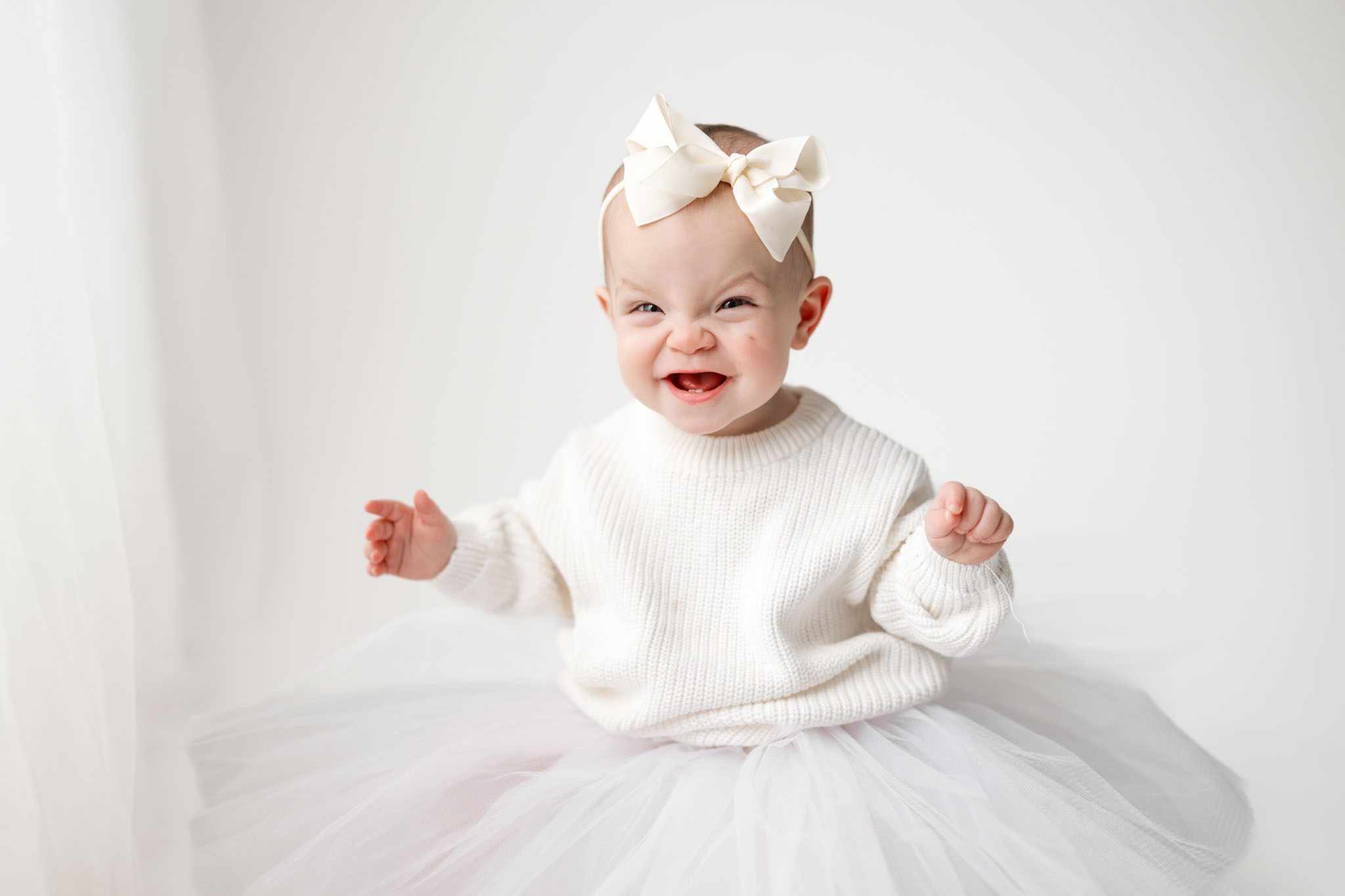 Toddler wearing a white knit sweater and tulle skirt for a formal first birthday portrait on a white background.