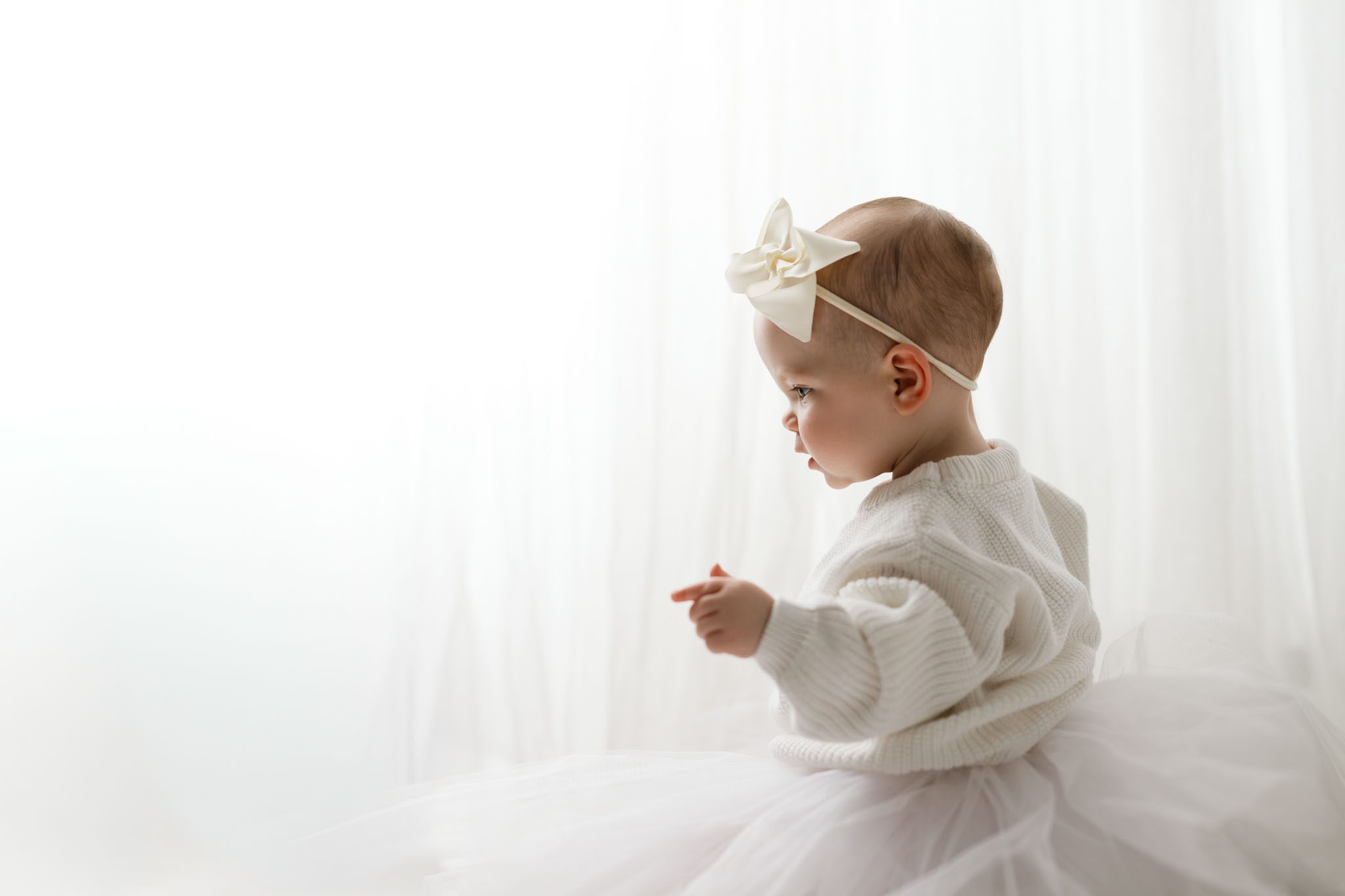Toddler wearing a white knit sweater and tulle skirt for a formal first birthday portrait on a white background.