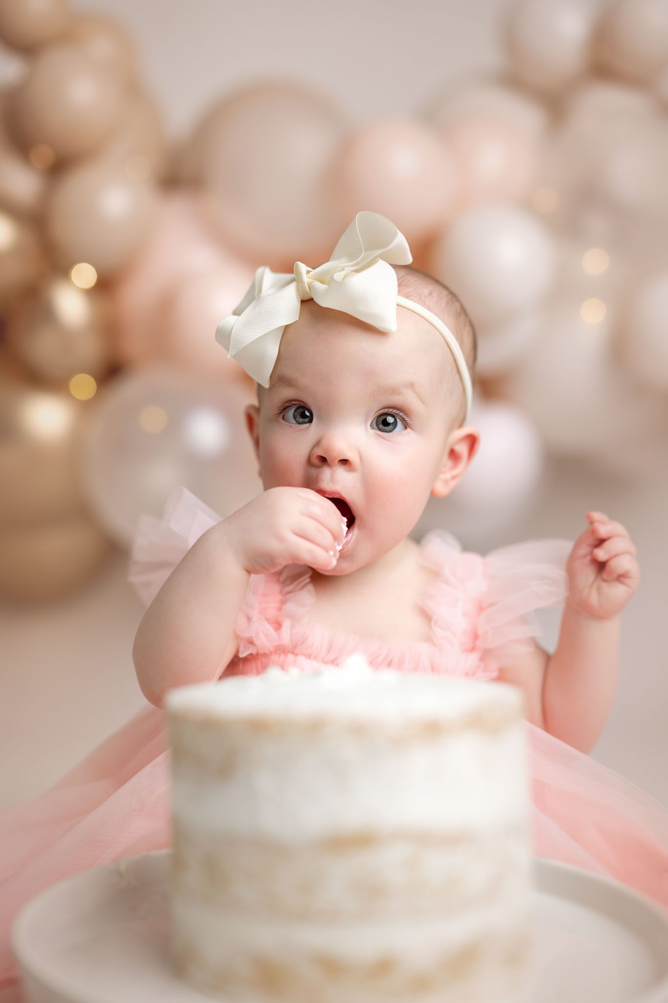 Baby girl sitting in front of pink and gold balloons during a first birthday cake smash session.