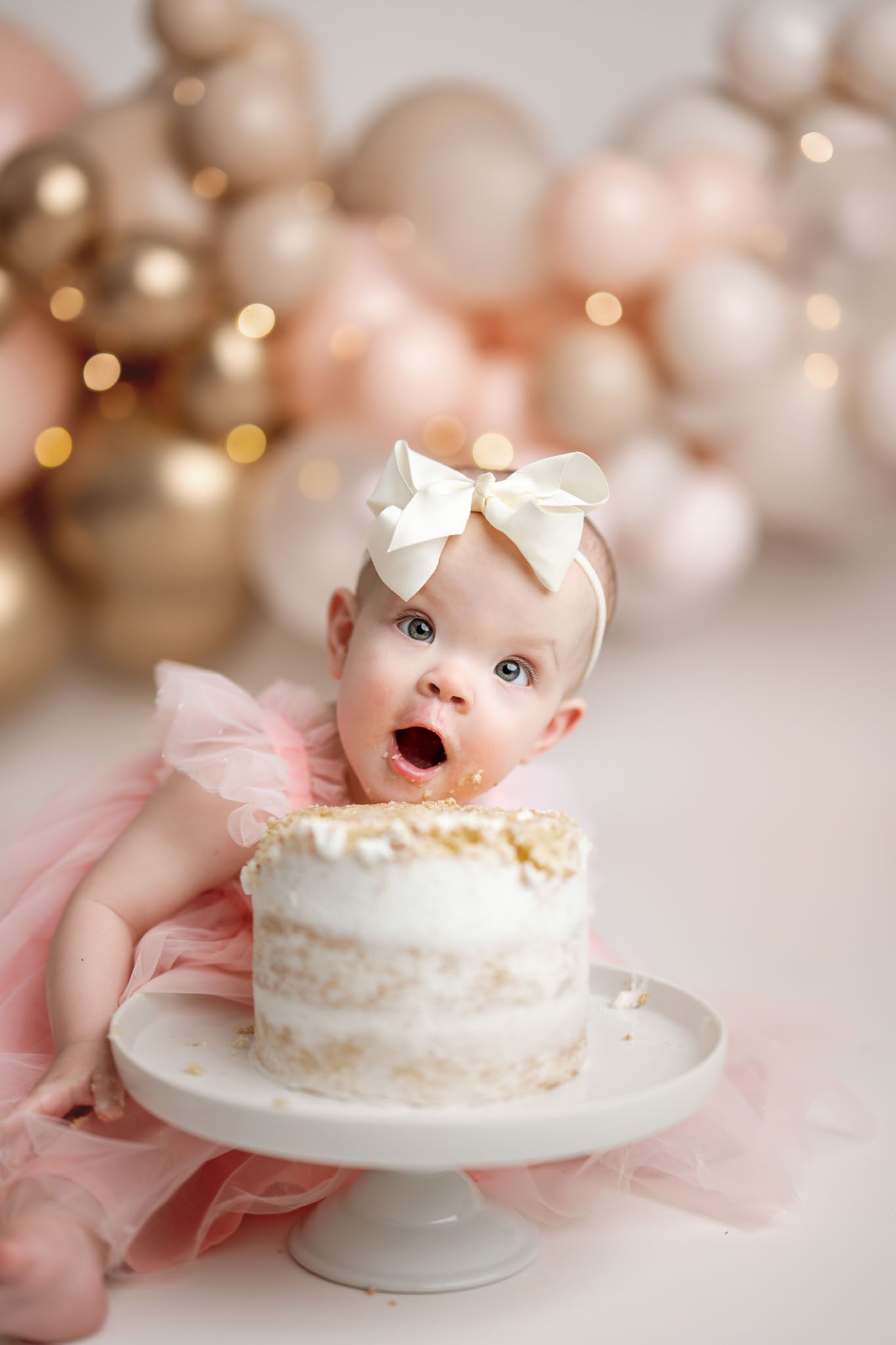 Baby girl sitting in front of pink and gold balloons during a first birthday cake smash session.