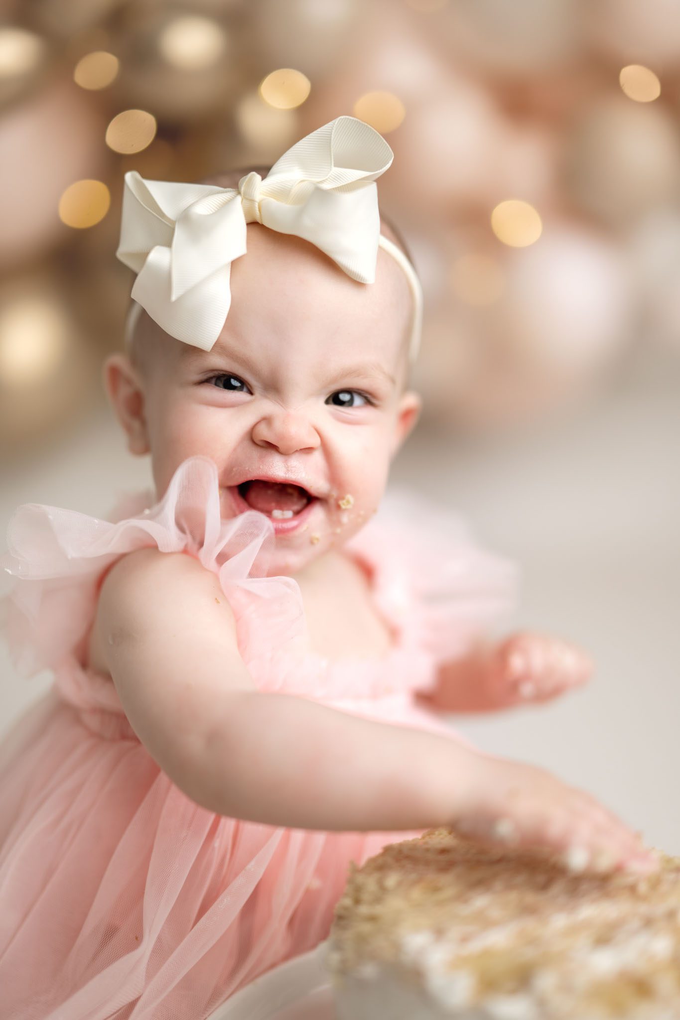 Close up of a one-year-old girl making a crinkled nose face with cake frosting on her hands.