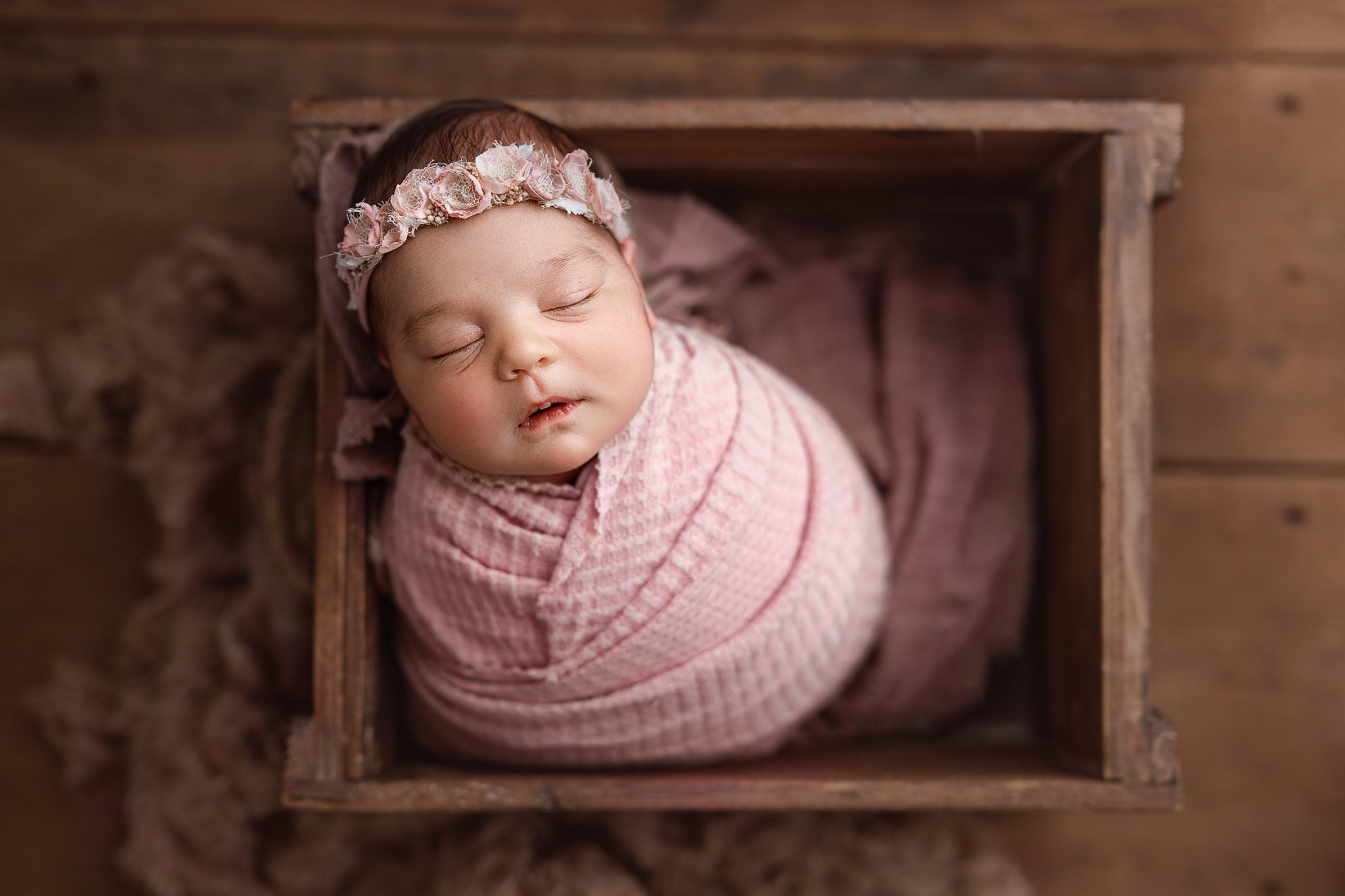A meticulously posed newborn baby girl sleeping in a custom-curated wooden crate with floral accents in a Scotch Plains photography studio.