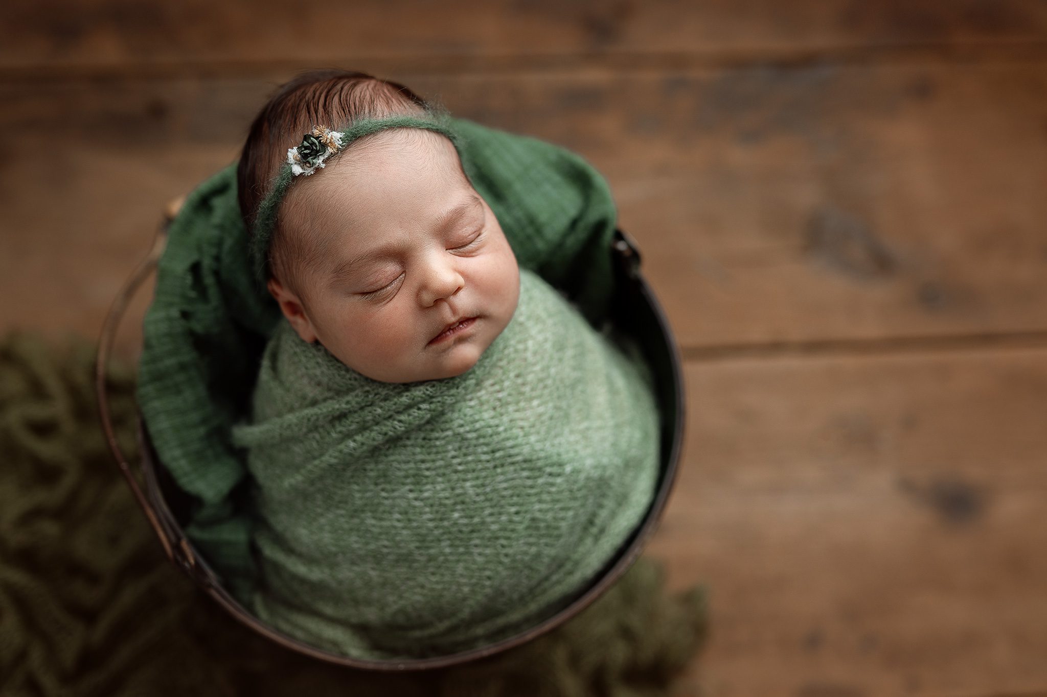A meticulously posed newborn baby girl sleeping in a custom-curated bucket in a Scotch Plains photography studio.