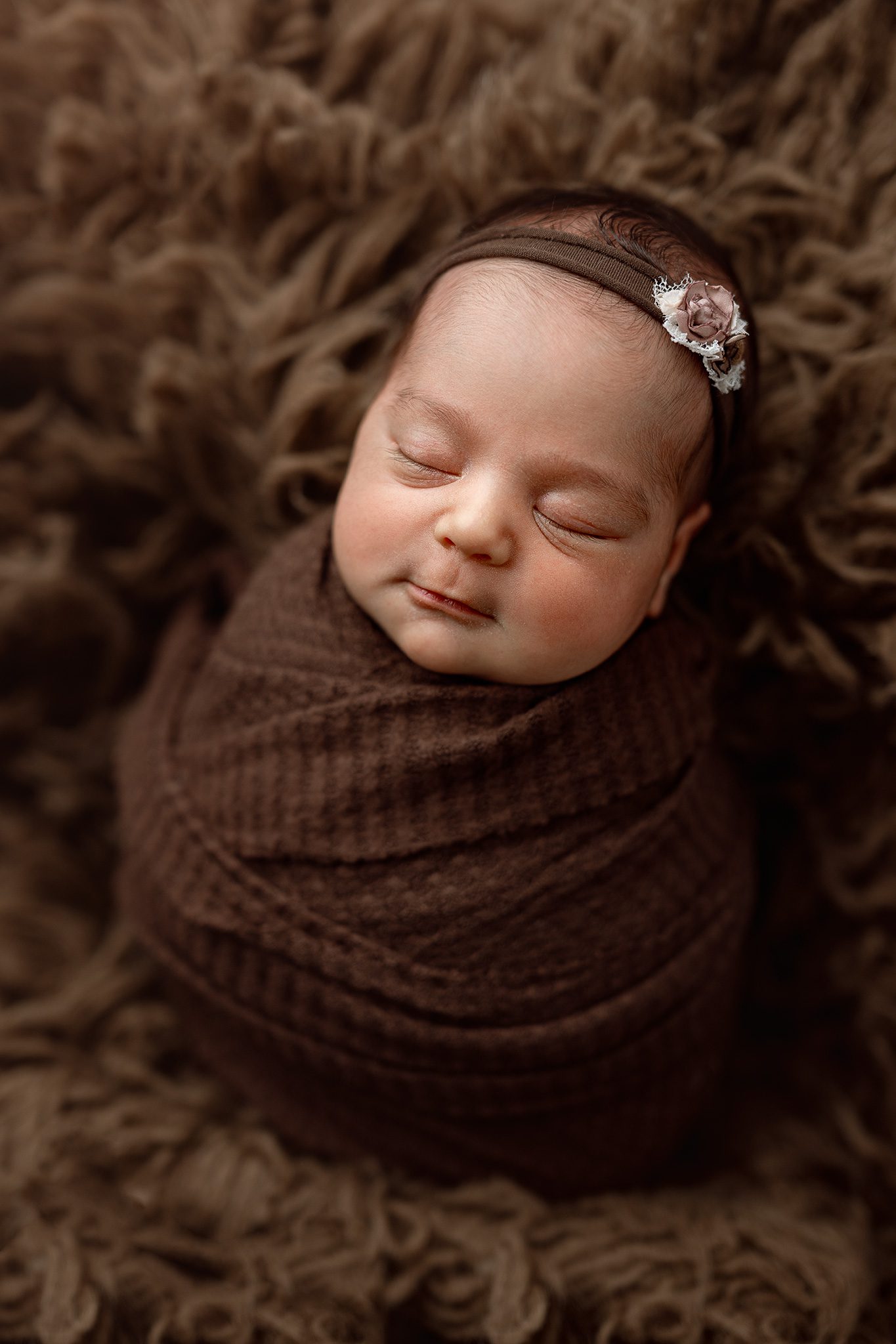 A meticulously posed newborn baby girl sleeping on a brown flokati in a Scotch Plains photography studio.