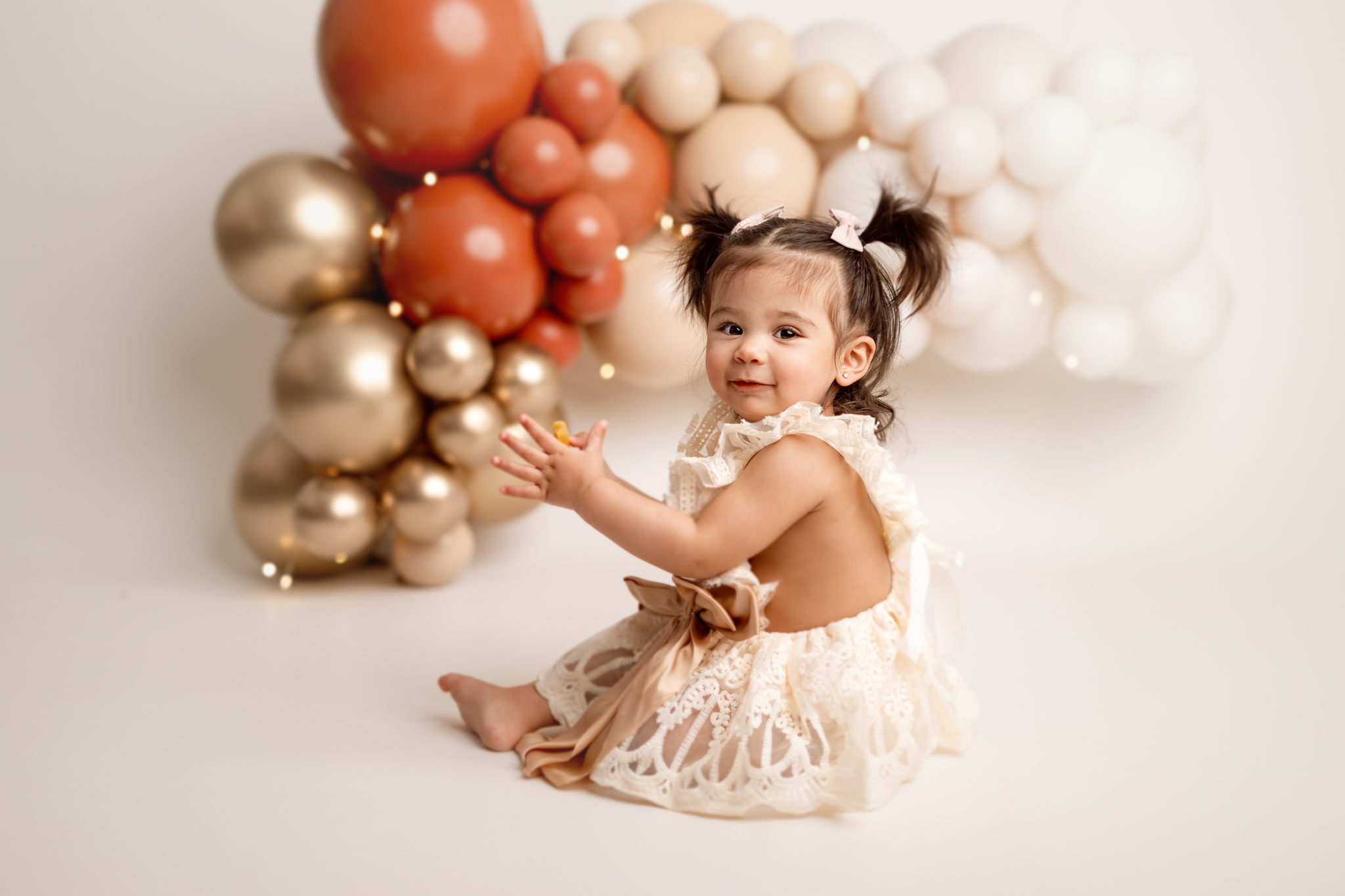 sweet little girl in her birthday dress claps hands infront of her balloon garland at her cake smash session