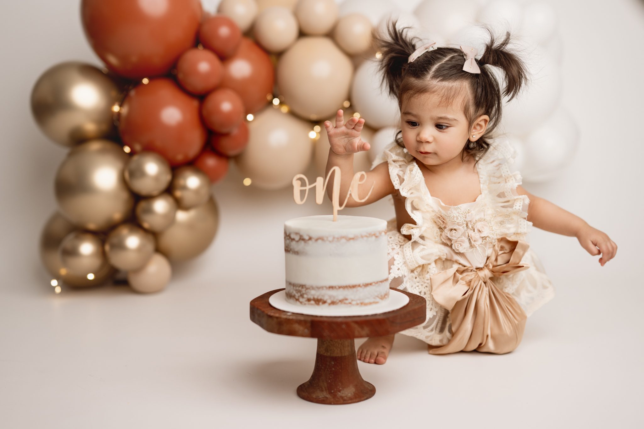 sweet little girl in her birthday dress smiles infront of her balloon garland at her cake smash session