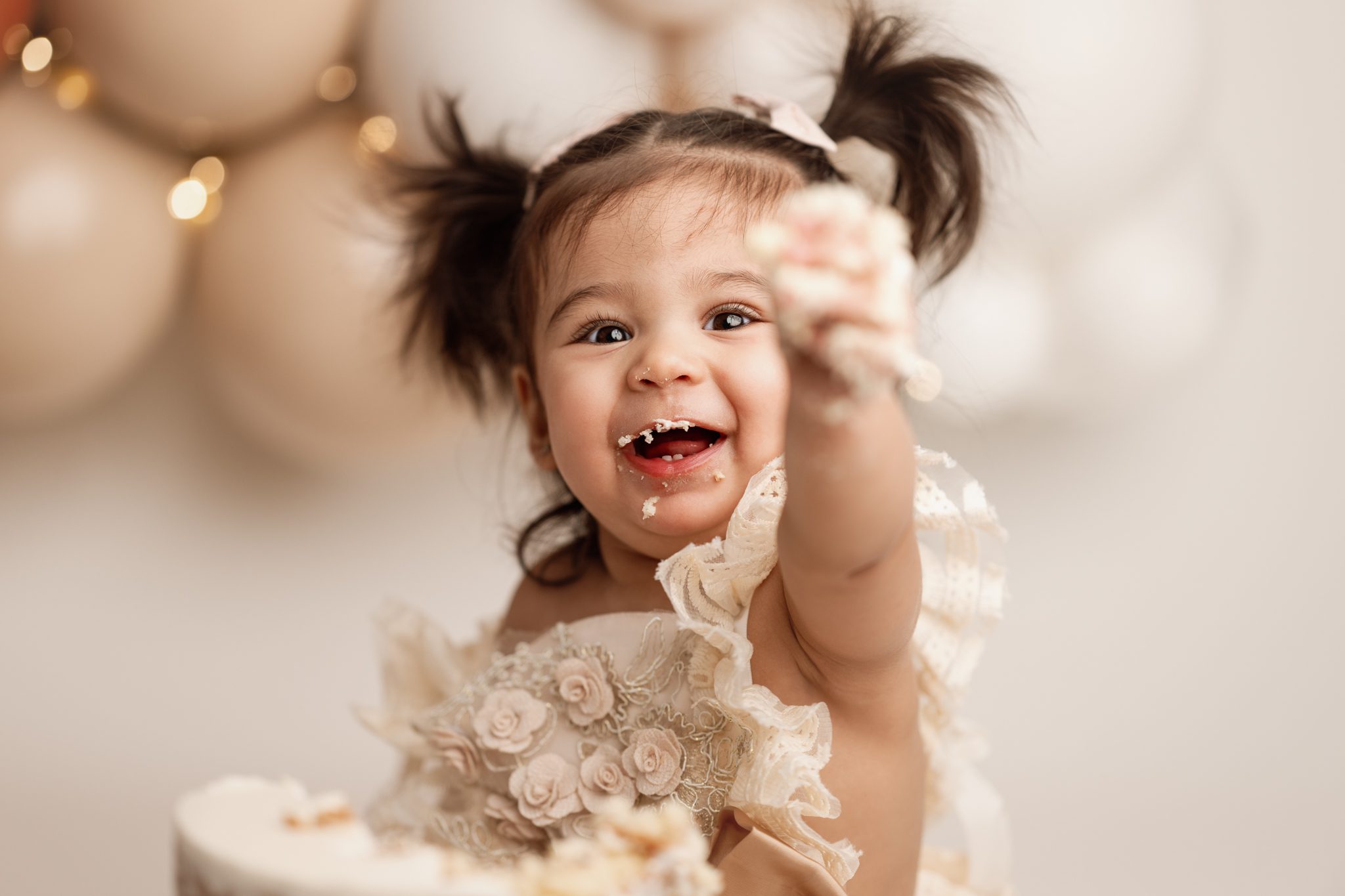 sweet little girl in her birthday dress smiles infront of her balloon garland at her cake smash session